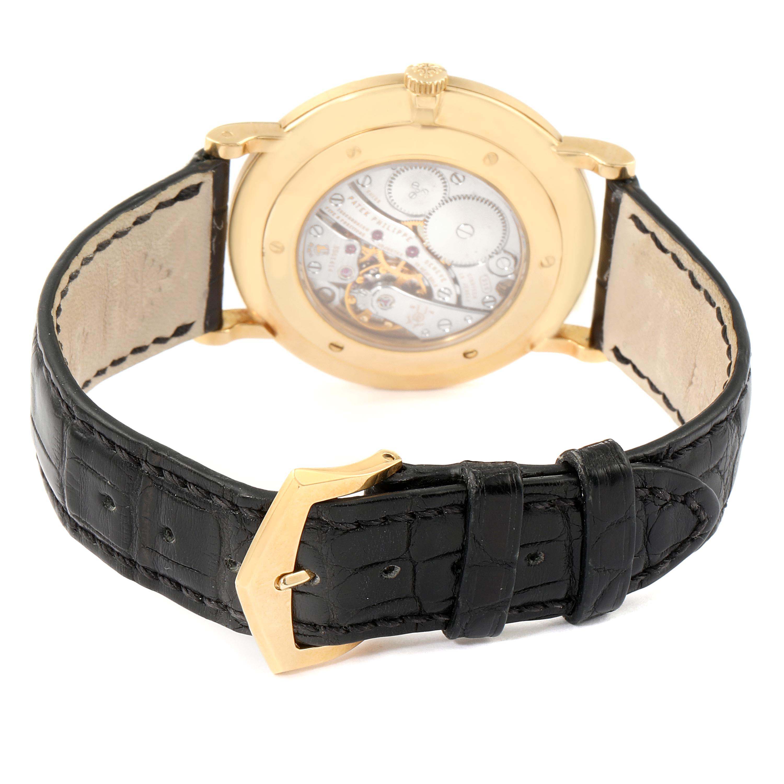 The image shows the back view of a Patek Philippe Calatrava 5119J Men's Yellow Gold White Dial 5119J Men's Yellow Gold White Dial watch, revealing the movement and black leather strap with a gold buckle.