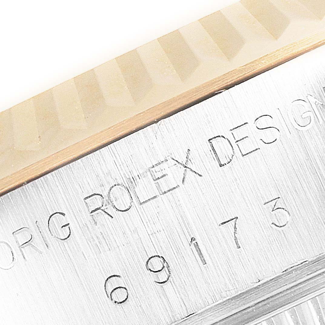 The image shows a close-up of the Rolex Datejust 69173 Women
s Steel and Gold (two tone) Champagne Dial 69173 Women
s Steel and Gold (two tone) Champagne Dial
s fluted bezel and part of the engraved casing.