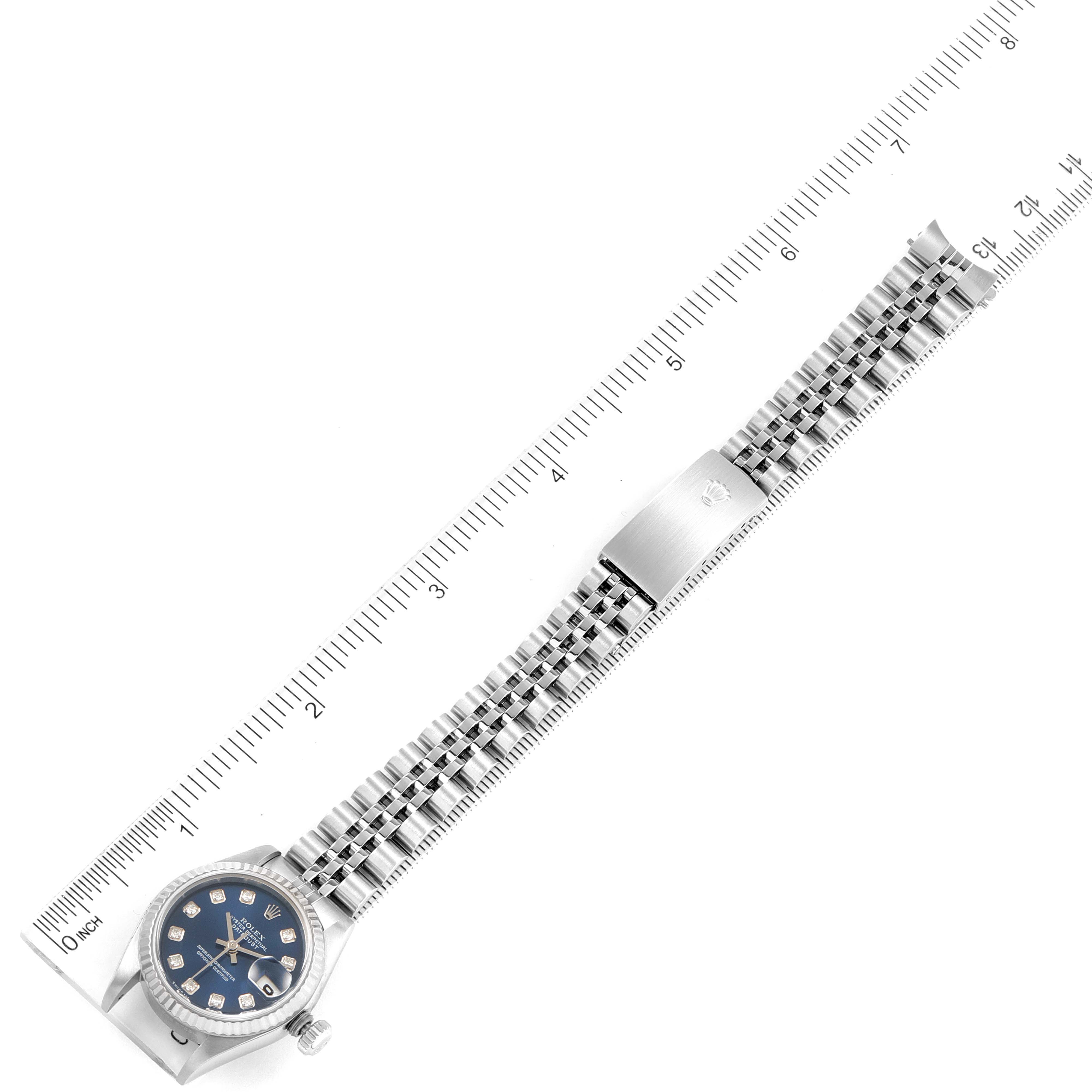 The Rolex Datejust 79174 Women
s Stainless Steel Blue Dial 79174 Women
s Stainless Steel Blue Dial watch is shown from a top-down angle, displaying the dial, bracelet, and clasp next to a ruler for scale.