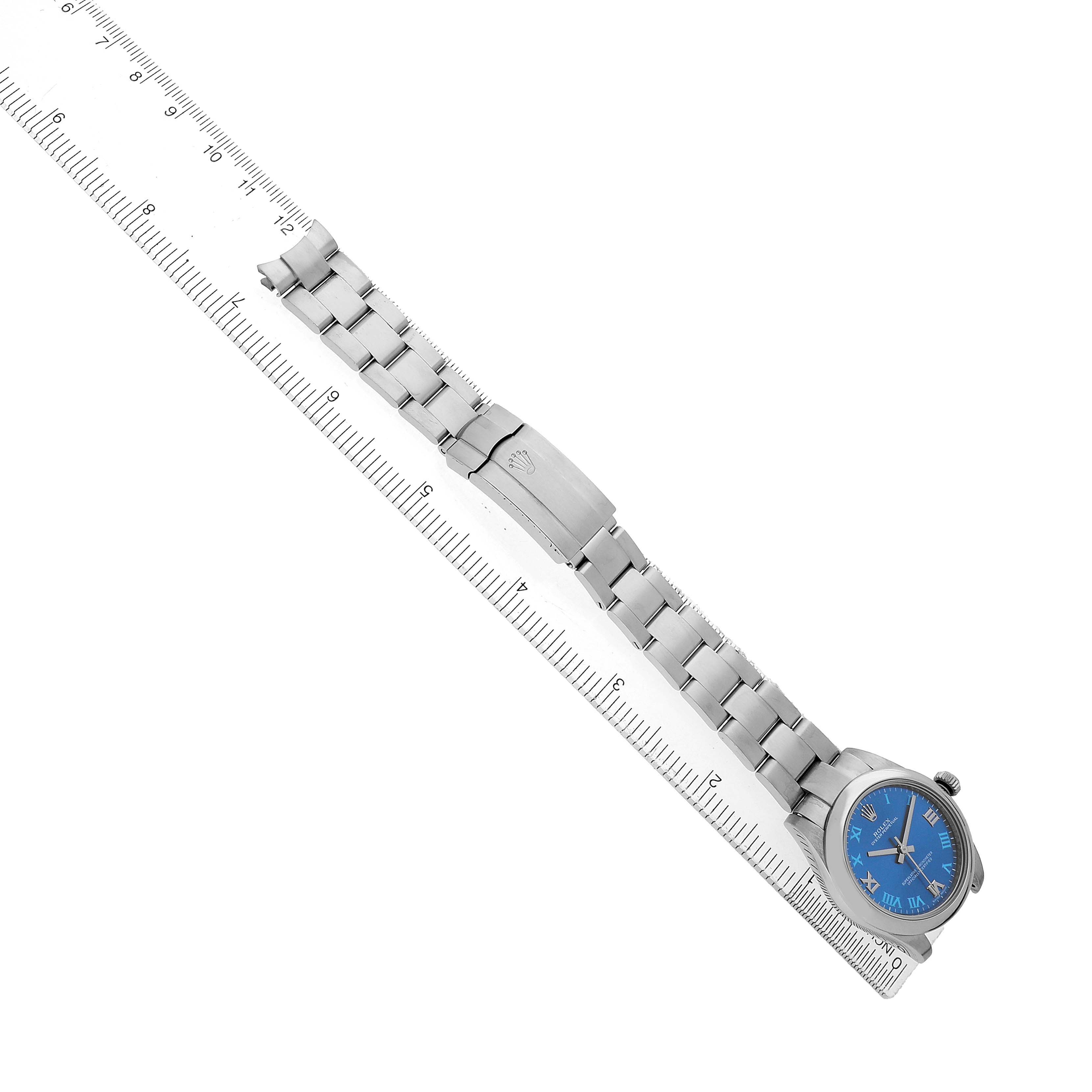 The Rolex Mid-Size 177200 Women's Stainless Steel Blue Dial watch is shown from a top-down angle, displaying the blue dial, bracelet, and clasp alongside a ruler.
