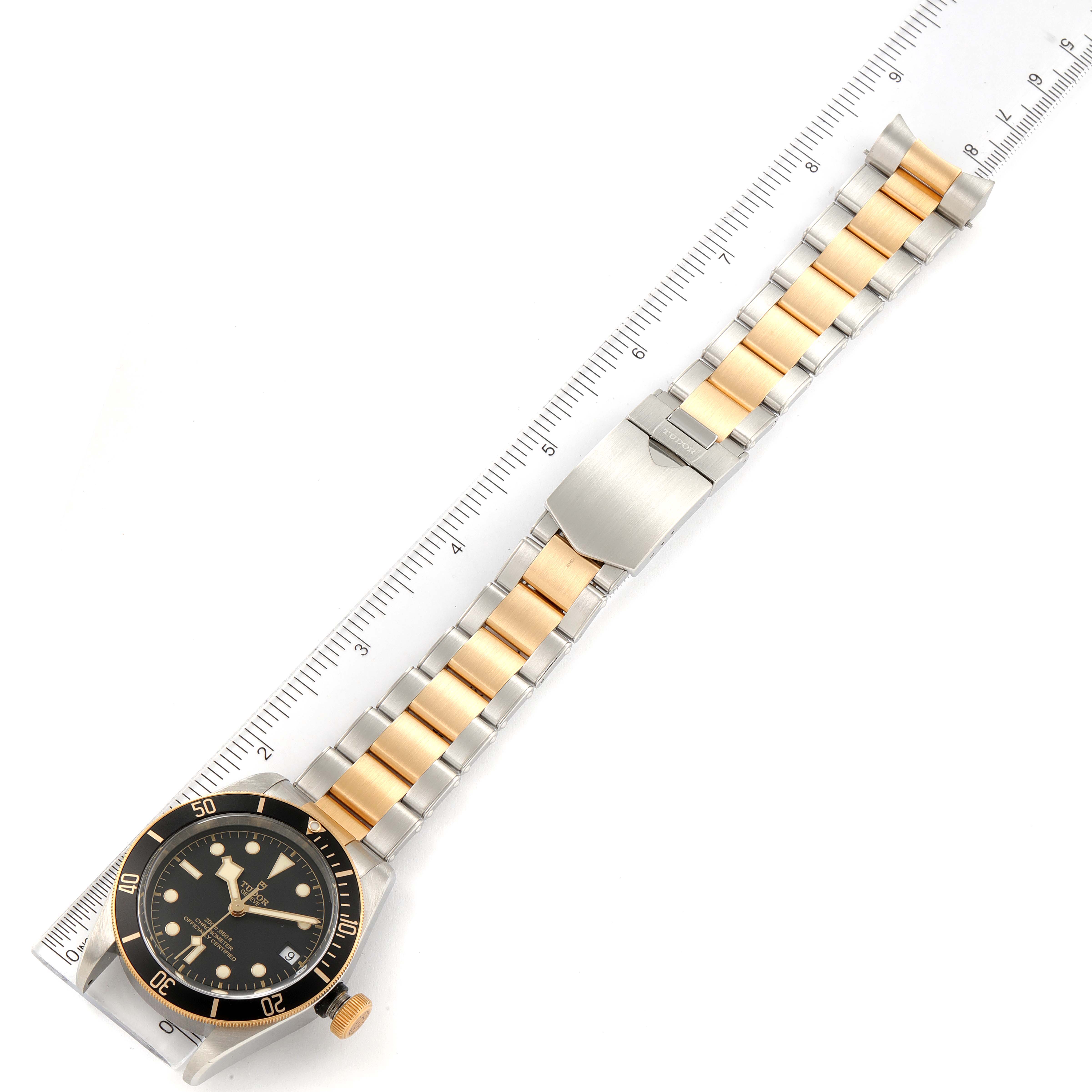 This image shows a Tudor Heritage Black Bay 79733 Men's Steel and Gold (two tone) Black Dial 79733 Men's Steel and Gold (two tone) Black Dial watch with a ruler, emphasizing the two-tone bracelet and clasp from a top-down angle.