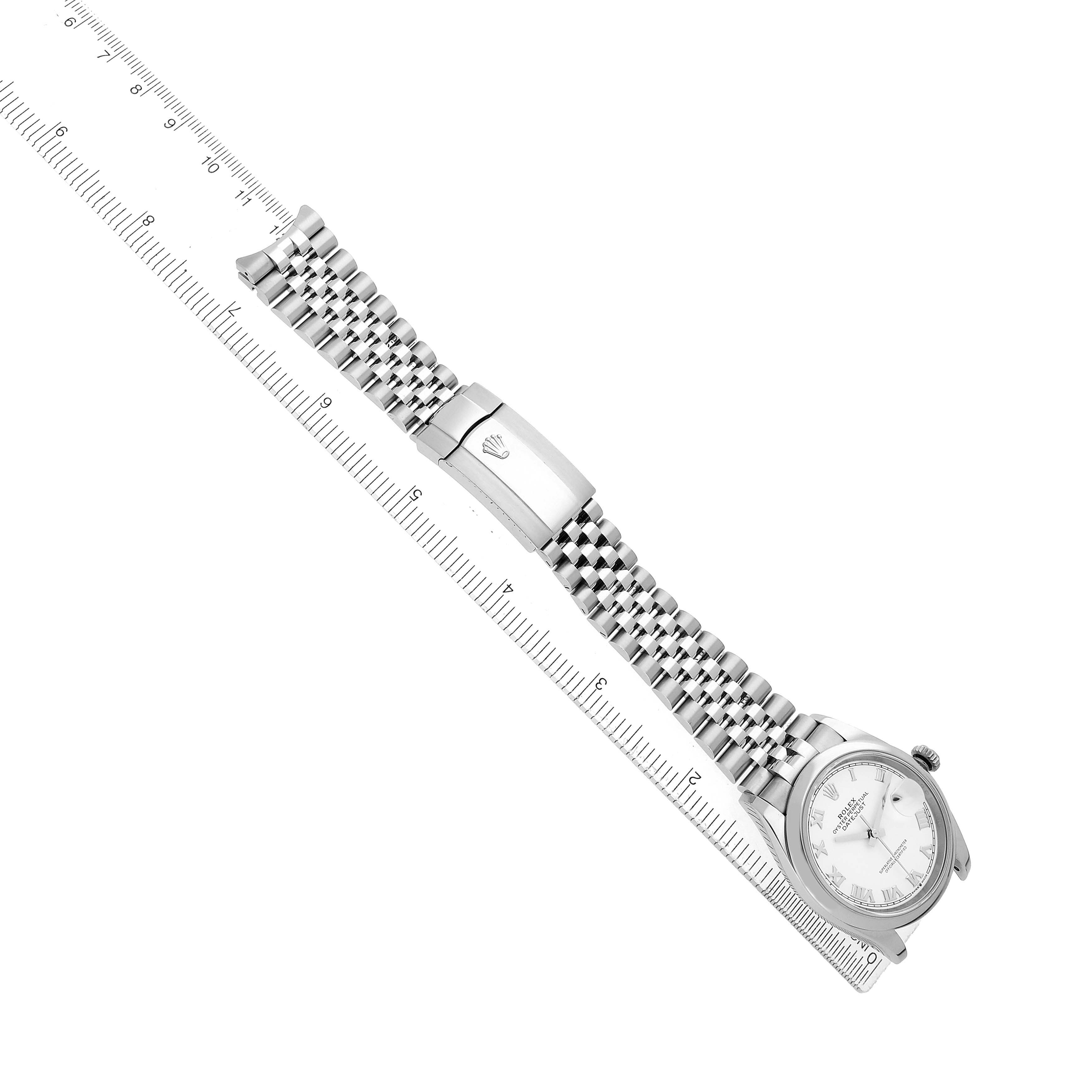 The Rolex Datejust 126200 Men's Stainless Steel White Dial watch is shown at an angle, displaying the face, bracelet, and clasp alongside a ruler for scale.