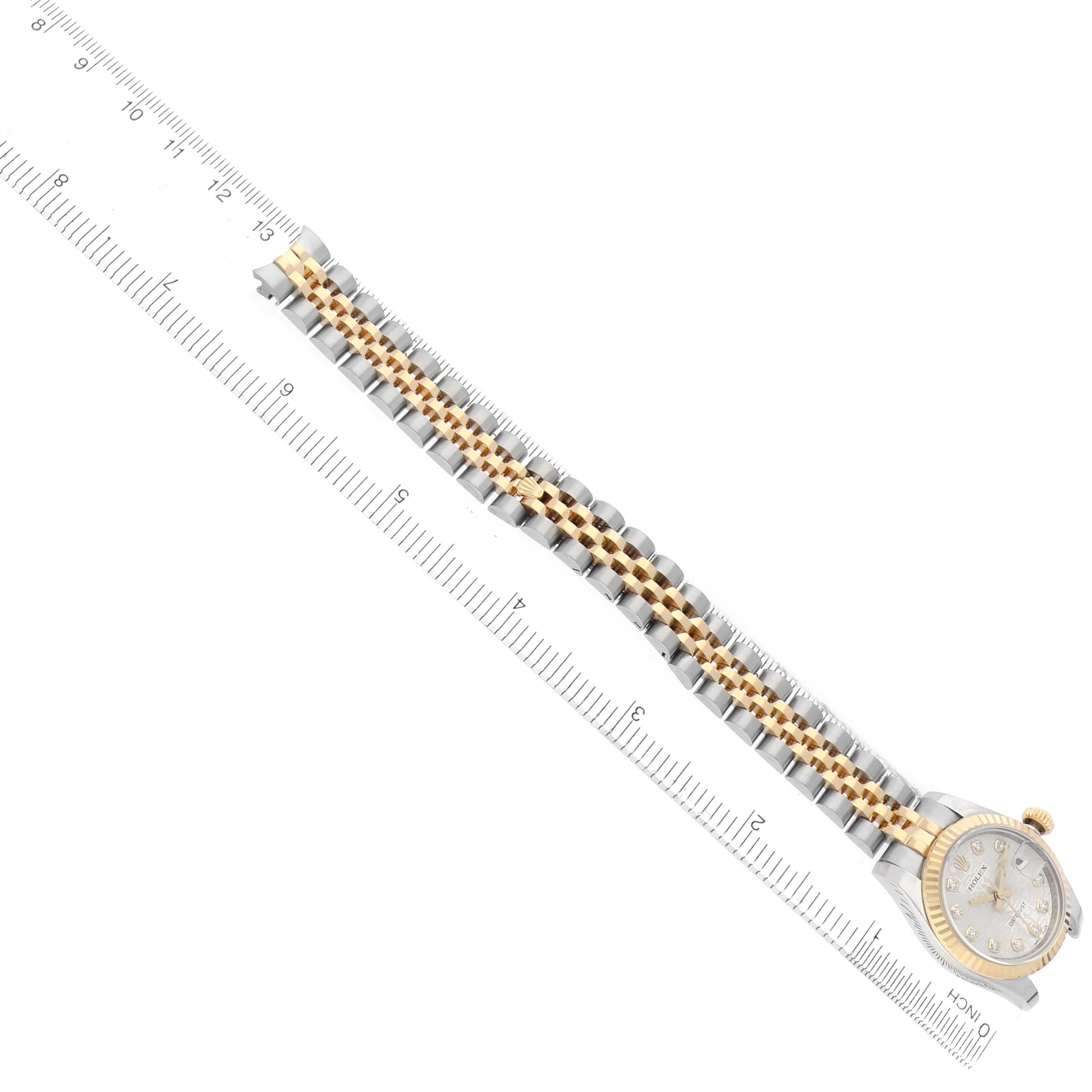 The Rolex Datejust 179173 Women's Steel and Gold (two tone) Silver Dial watch is shown diagonally, highlighting the face, bezel, and two-tone bracelet alongside a ruler.