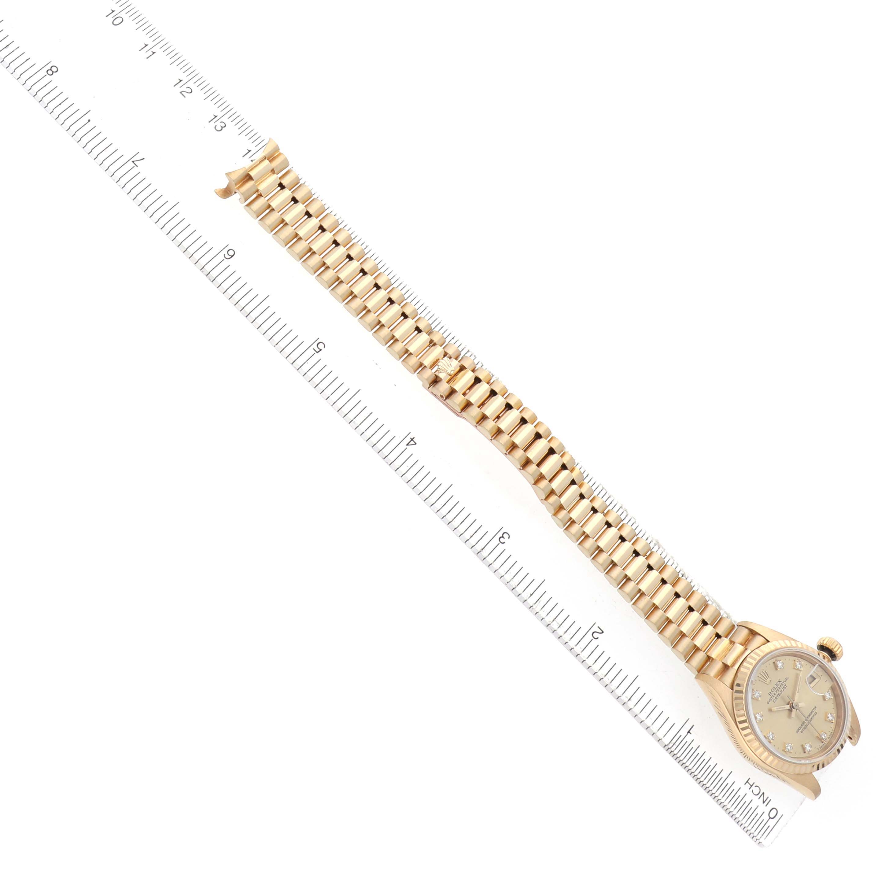 The Rolex President 69178 Women's Yellow Gold Champagne Dial watch is shown from a top view, featuring its gold bracelet and face alongside a ruler.