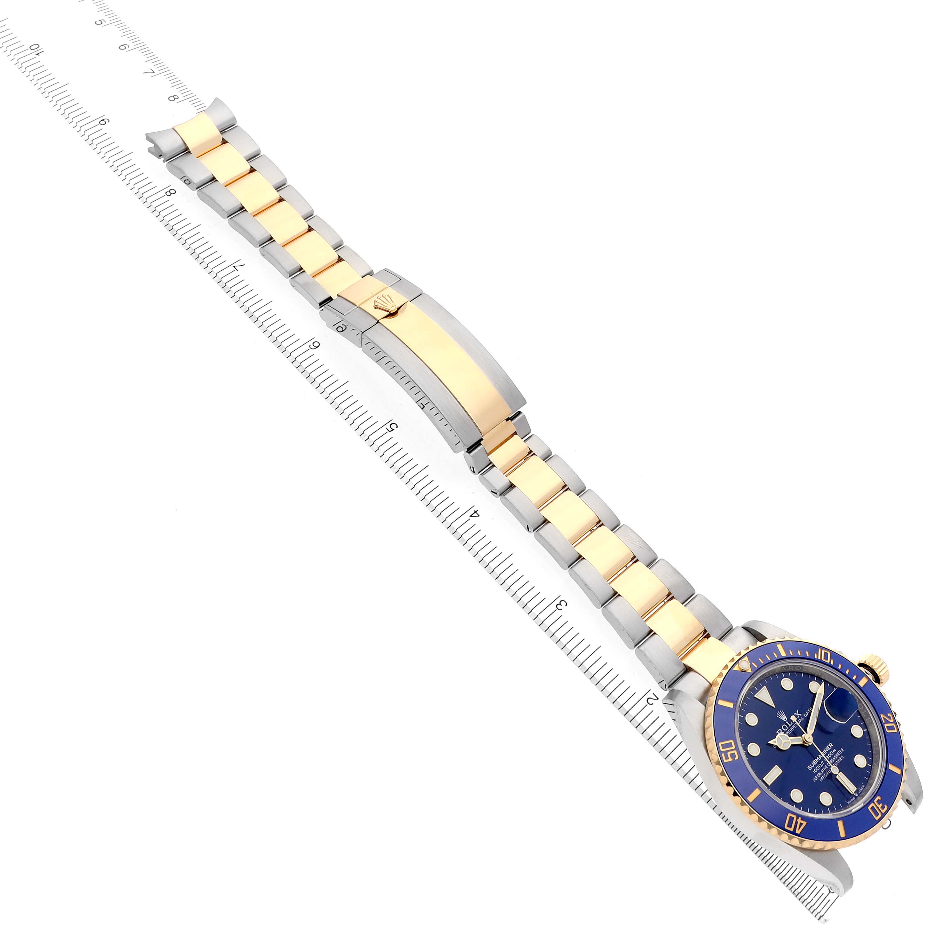 The Rolex Submariner 126613LB Men's Steel and Gold (two tone) Blue Dial 126613LB Men's Steel and Gold (two tone) Blue Dial watch is displayed at an angle showcasing its blue face, bezel, and two-tone bracelet alongside a ruler.