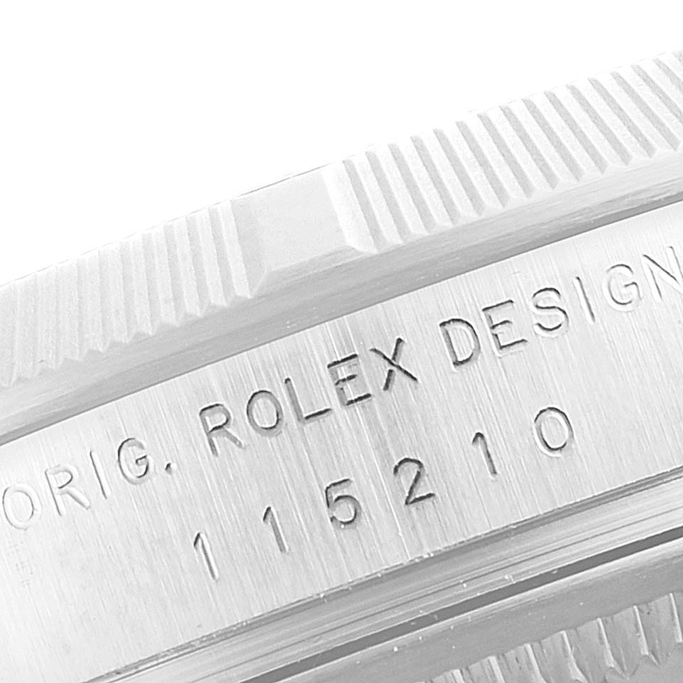 The image shows a close-up of the serial number engraving and bezel of a Rolex Date 115210 Men's Stainless Steel Silver Dial 115210 Men's Stainless Steel Silver Dial model.