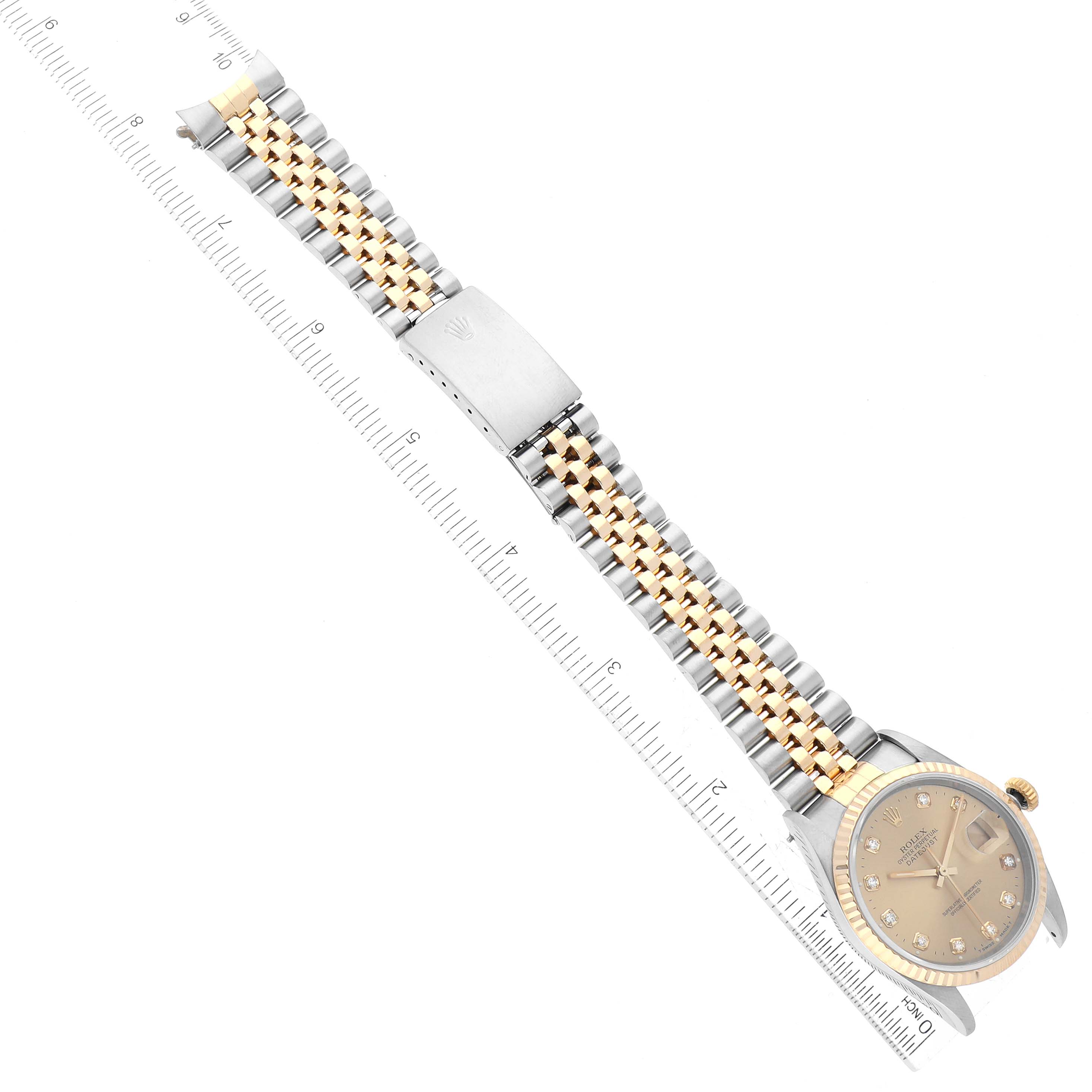 A Rolex Datejust 16233 Men's Steel and Gold (two tone) Champagne Dial 16233 Men's Steel and Gold (two tone) Champagne Dial watch is shown flat with a view of its dial and metal bracelet along a ruler for size reference.