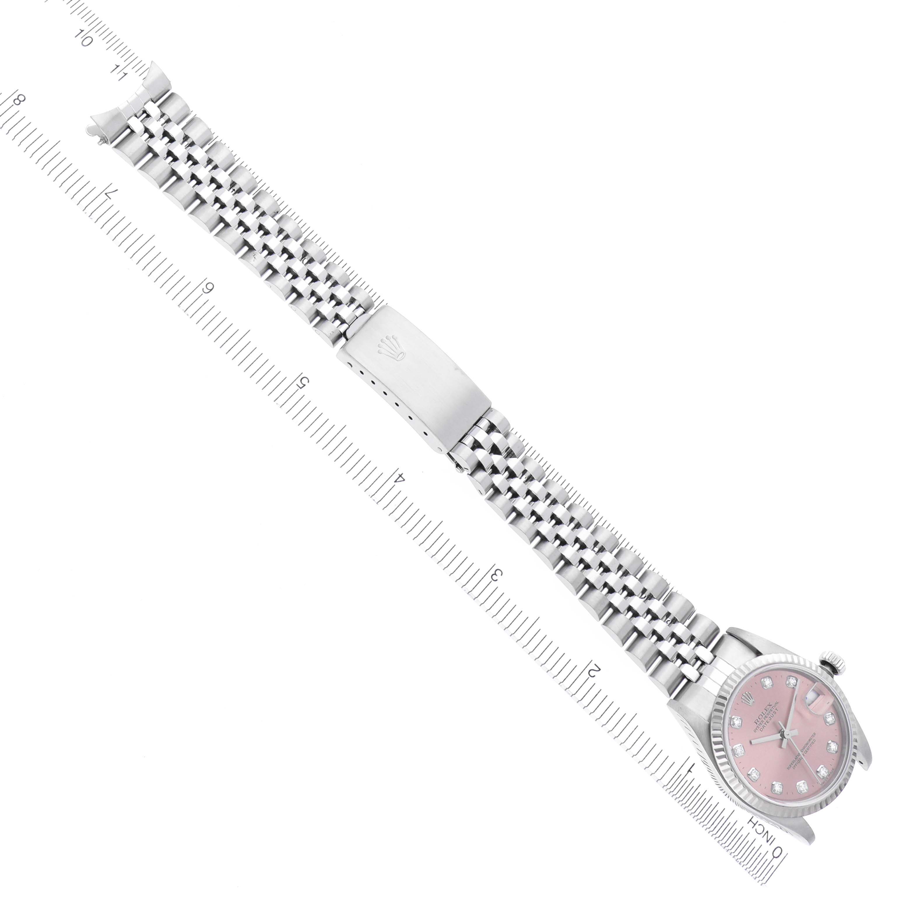 The Rolex Mid-Size 78274 Women's Stainless Steel Pink Dial 78274 Women's Stainless Steel Pink Dial watch is shown from a top-down angle, displaying its pink dial and silver bracelet fully extended alongside a ruler.