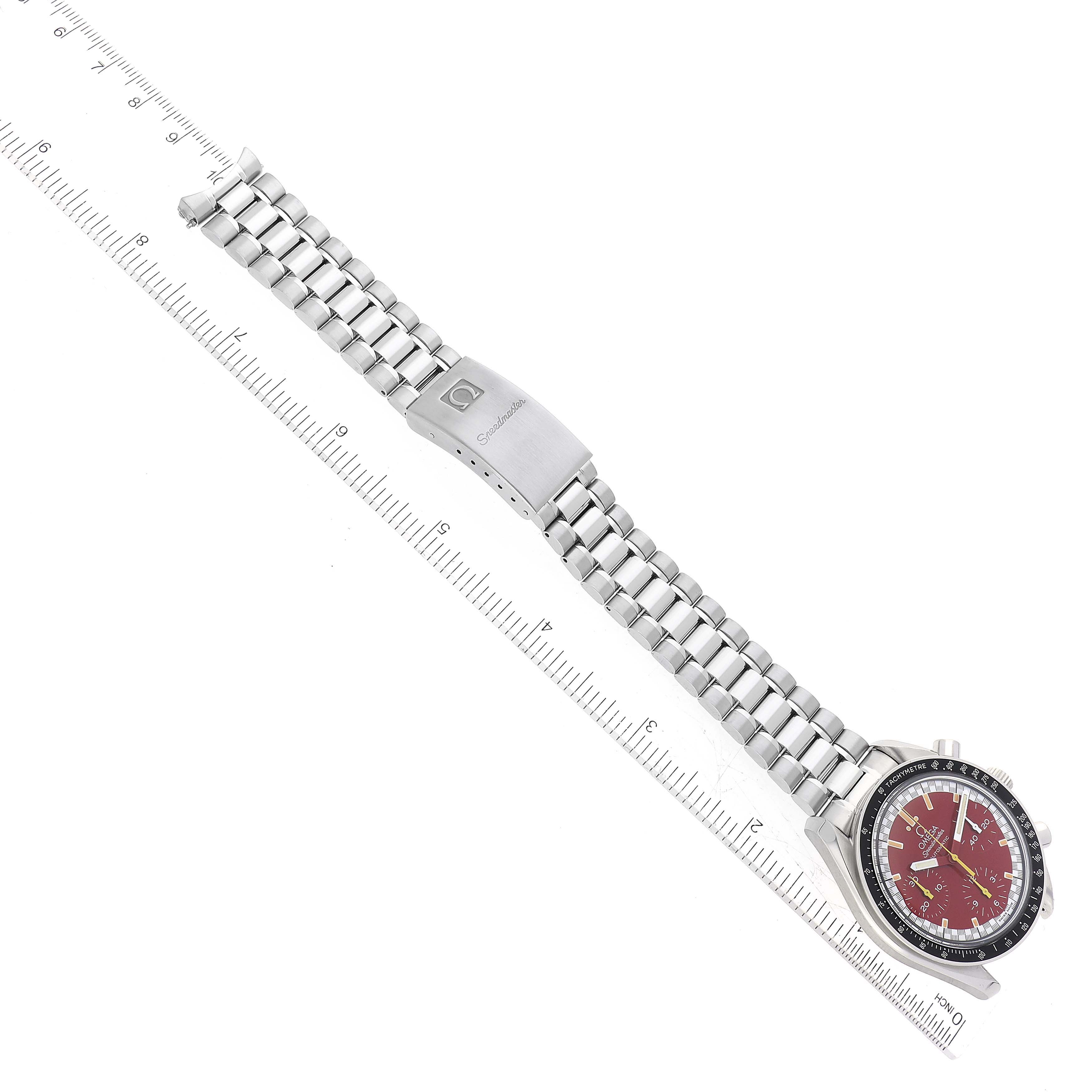 The Omega Speedmaster 3510.61.00 Men
s Stainless Steel Red Dial 3510.61.00 Men
s Stainless Steel Red Dial watch is shown flat with its stainless steel bracelet and clasp visible, alongside a measuring scale.
