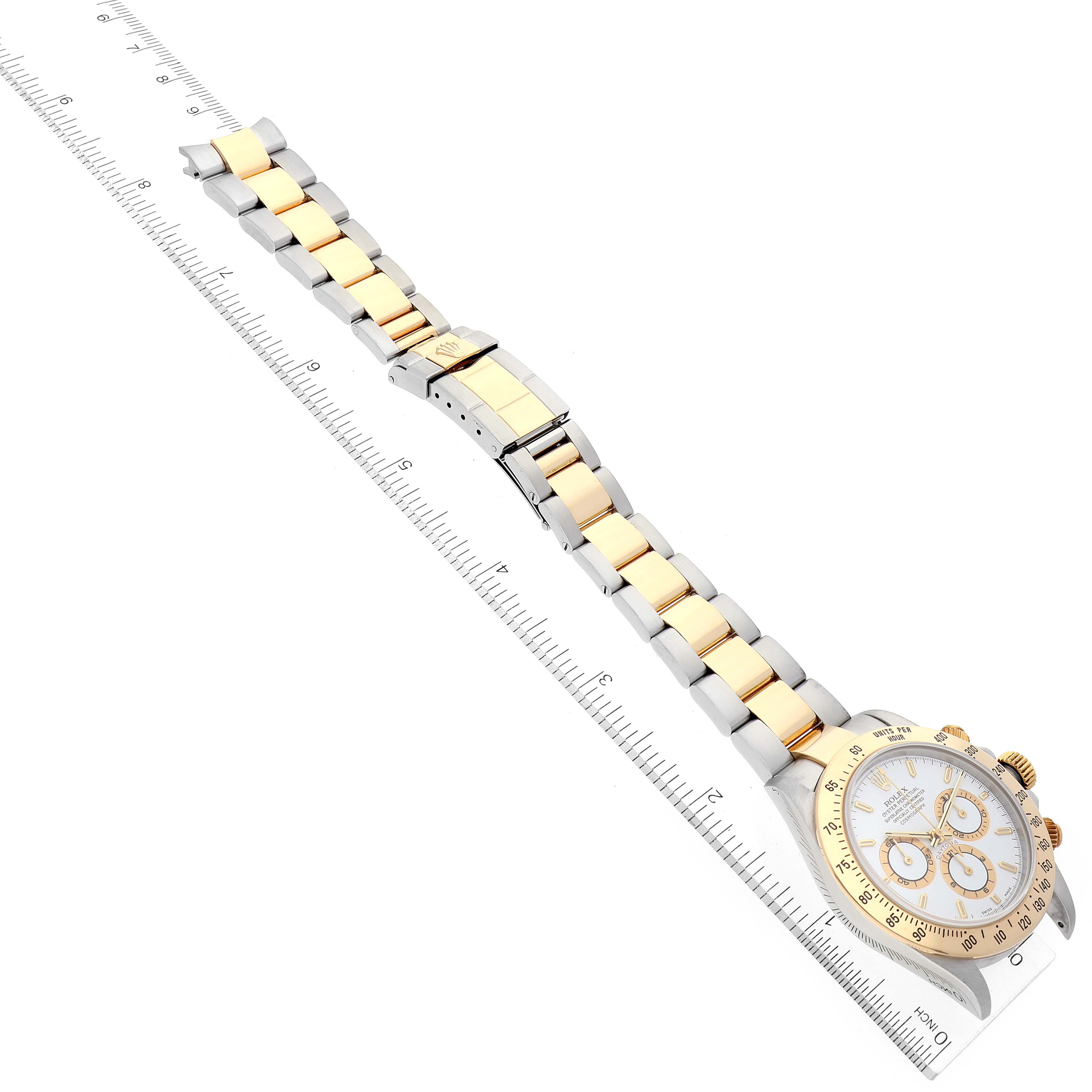 The image shows a Rolex Daytona 16523 Men's Steel and Gold (two tone) White Dial 16523 Men's Steel and Gold (two tone) White Dial watch laid flat, with a clear view of the band, clasp, and face, next to a ruler for scale.