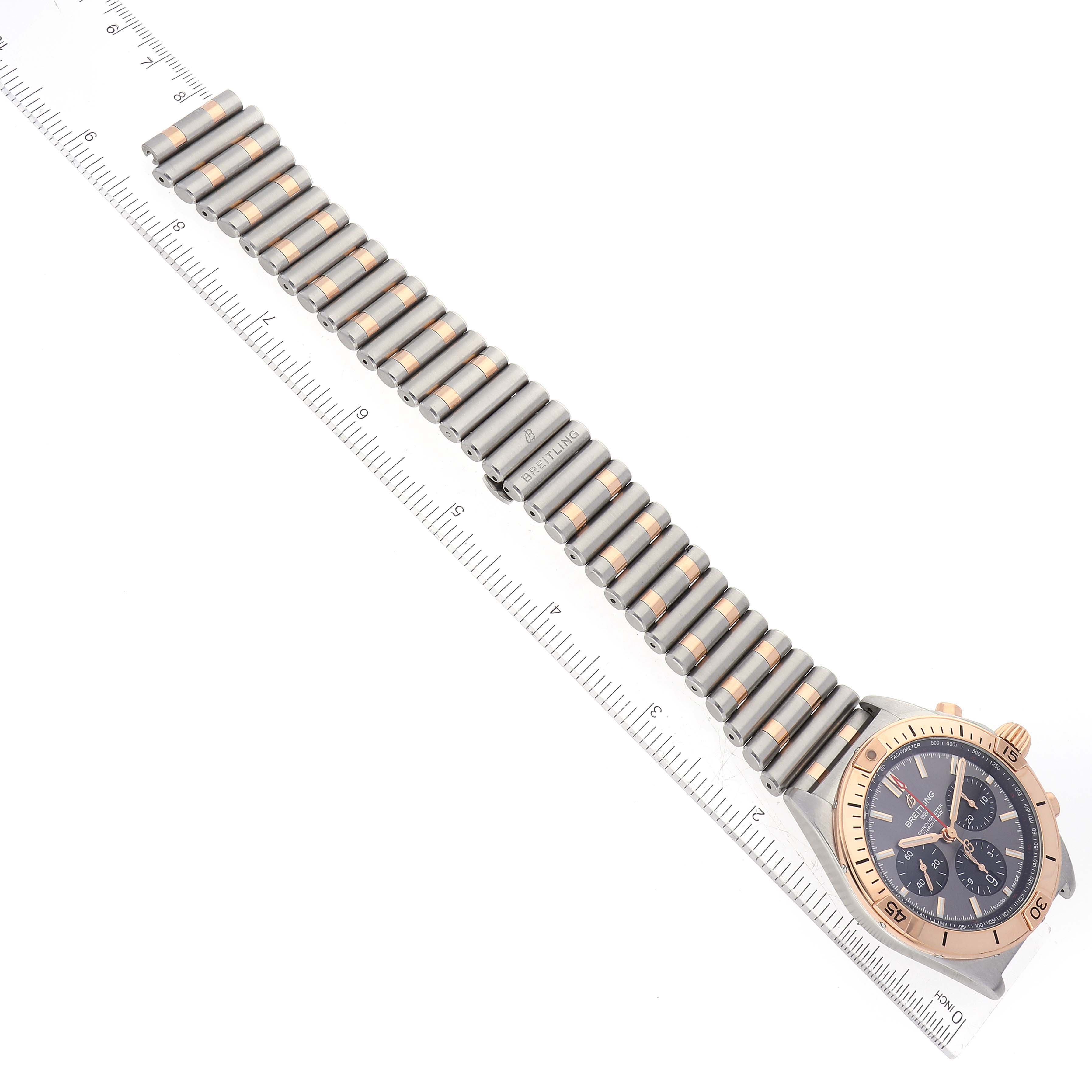The image shows an overhead view of the Breitling Chronomat UB0134 Men's Steel and Gold (two tone) Grey Dial UB0134 Men's Steel and Gold (two tone) Grey Dial watch, with the watch face, bezel, and band visible along a ruler.