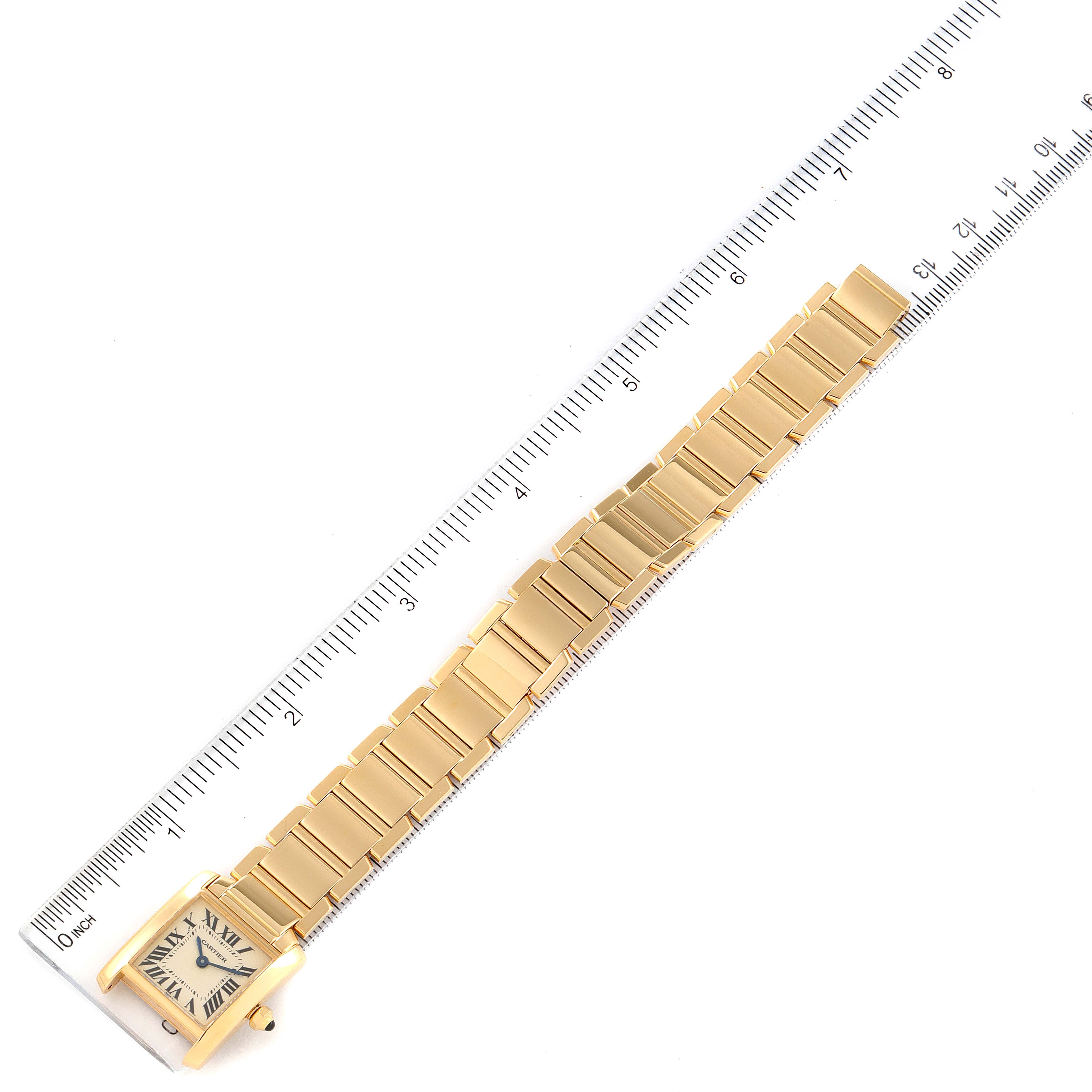 The image shows a gold Cartier Tank Française watch placed alongside a ruler, viewed from above.