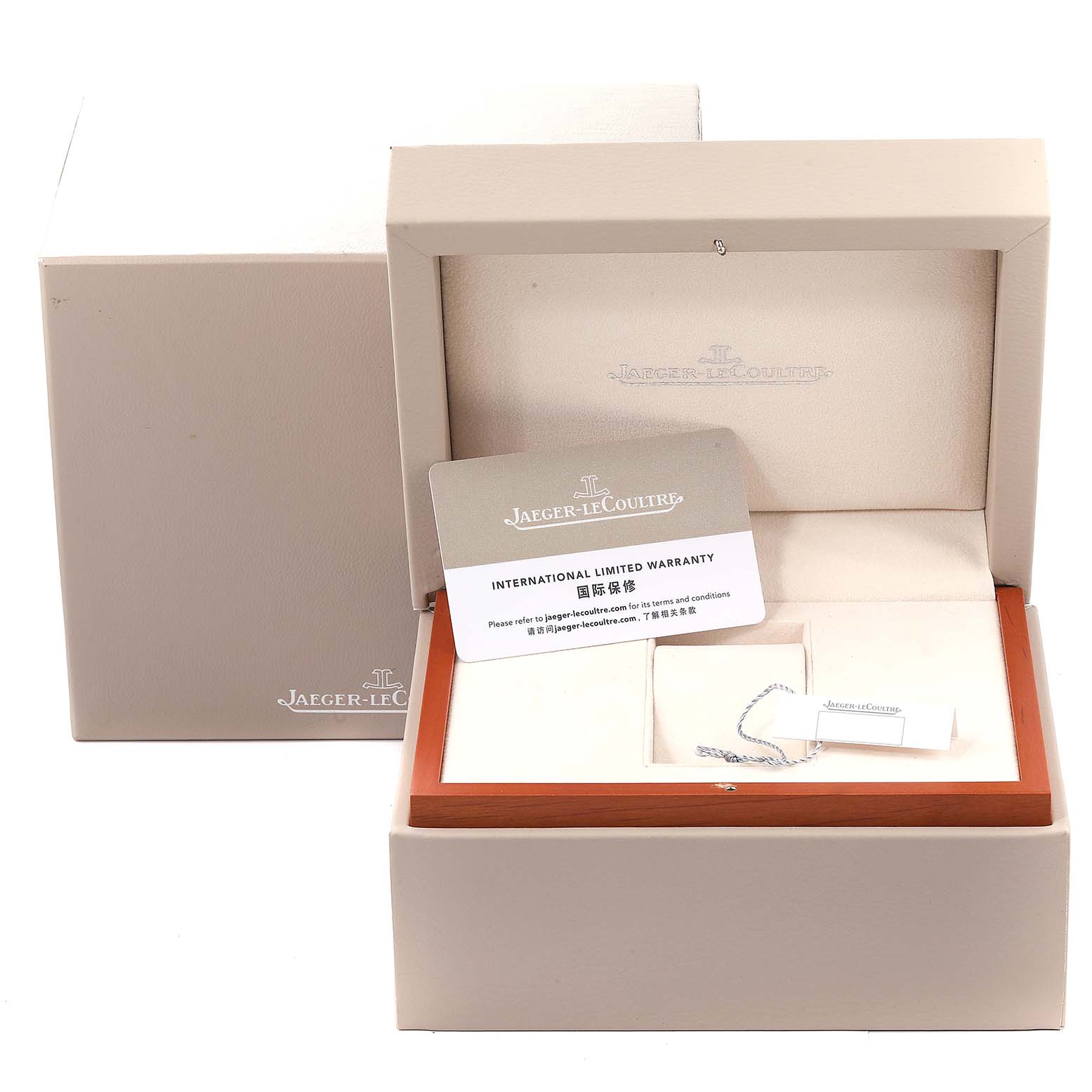 The image shows the packaging of a Jaeger-LeCoultre Reverso watch, including the box, warranty card, and a small tag.