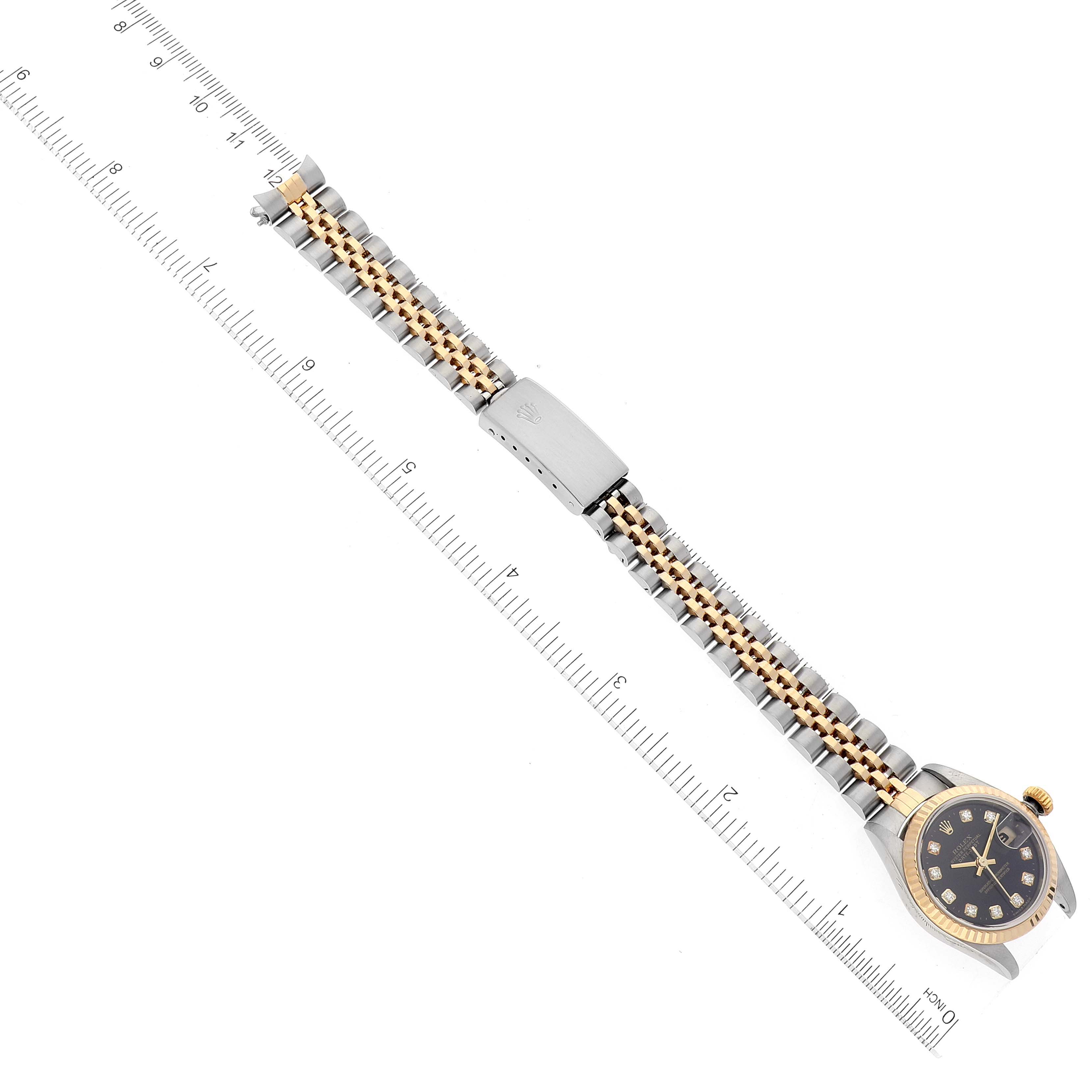 The image shows an overhead view of a Rolex Datejust 79173 Women's Steel and Gold (two tone) Black Dial 79173 Women's Steel and Gold (two tone) Black Dial watch with its bracelet and clasp laid flat, alongside a ruler for scale.