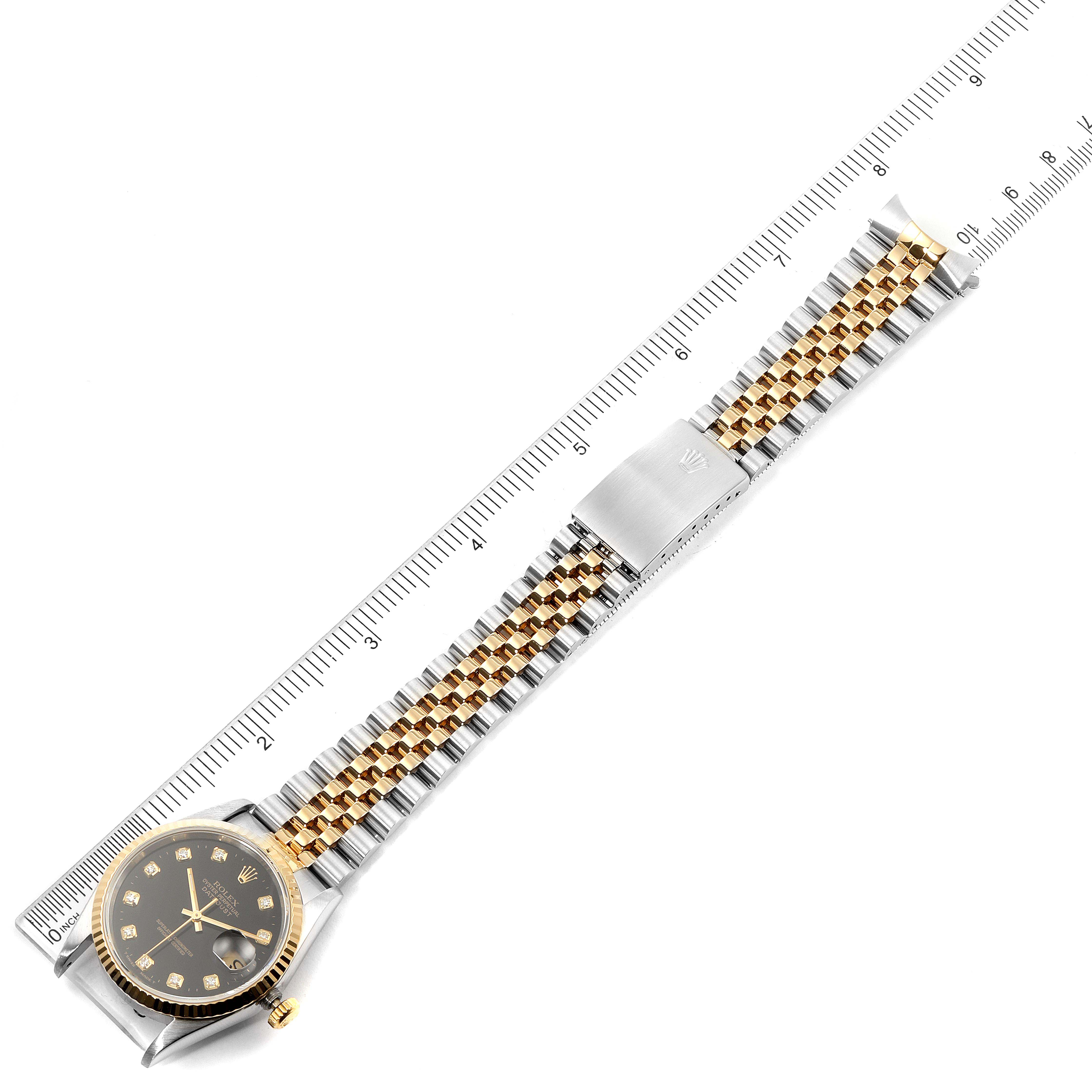 This image shows a Rolex Datejust 16233 Men
s Steel and Gold (two tone) Black Dial 16233 Men
s Steel and Gold (two tone) Black Dial watch from a top view, displaying the face, bracelet, and clasp alongside a ruler.
