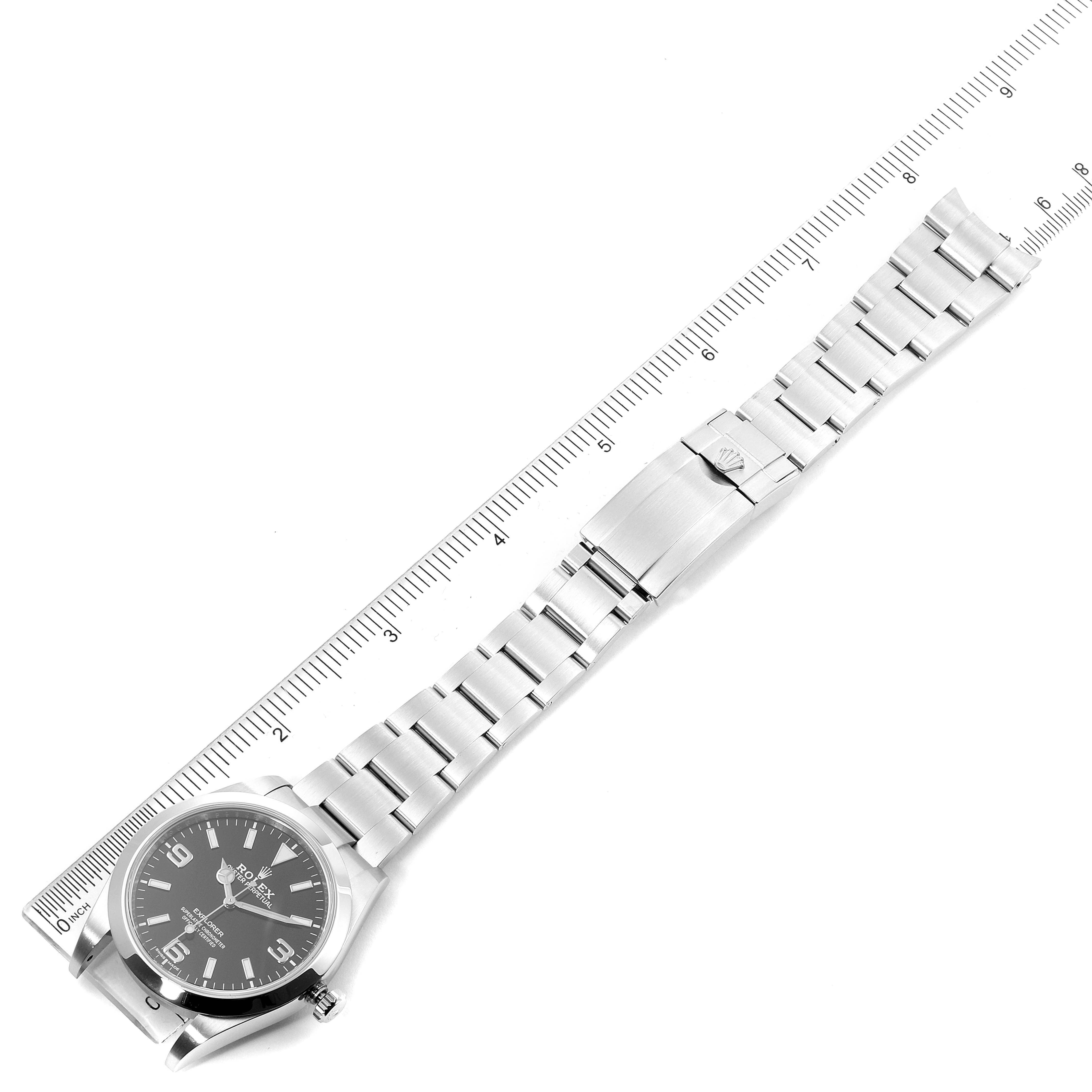 The image shows a full view of a Rolex Explorer 214270 Men
s Stainless Steel Black Dial 214270 Men
s Stainless Steel Black Dial model watch laid flat with a ruler beside it for scale.