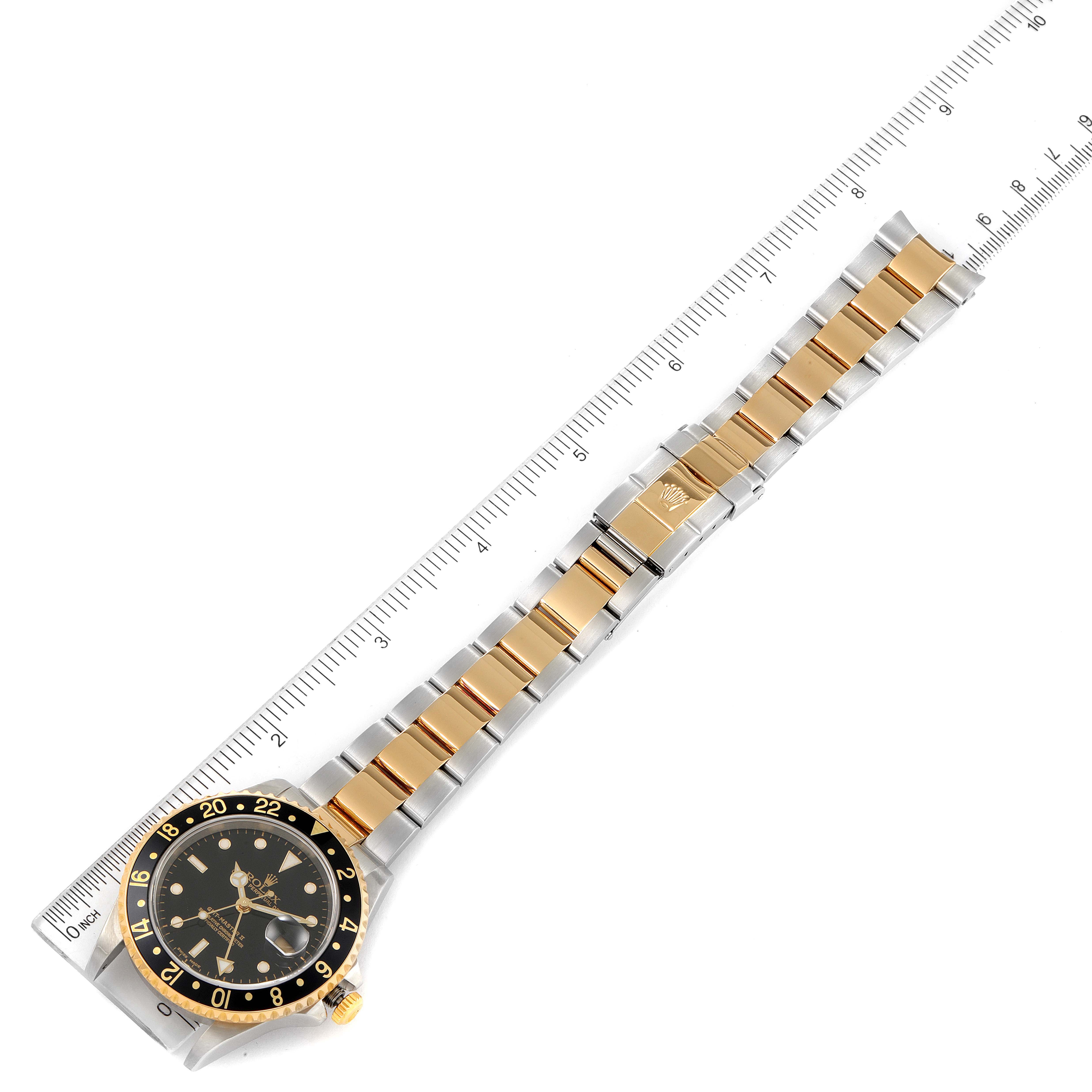 The image shows a top-down view of a Rolex GMT-Master 16713 Men's Steel and Gold (two tone) Black Dial 16713 Men's Steel and Gold (two tone) Black Dial watch, highlighting its dial, bezel, bracelet, and clasp next to a ruler.