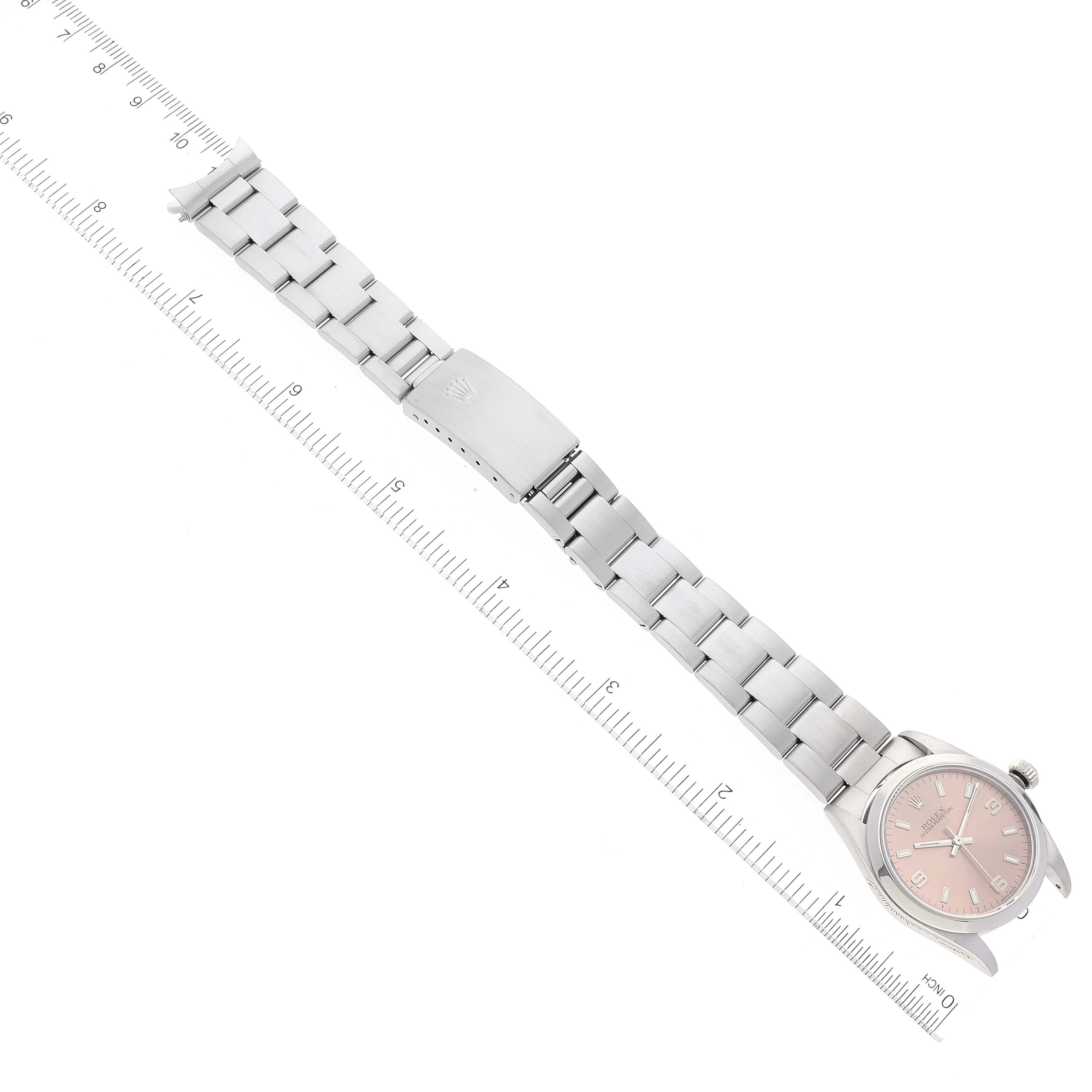 The image shows a top-down view of the Rolex Mid-Size 77080 Women
s Stainless Steel Pink Dial 77080 Women
s Stainless Steel Pink Dial watch, displaying the face, band, clasp, and part of a ruler for scale.