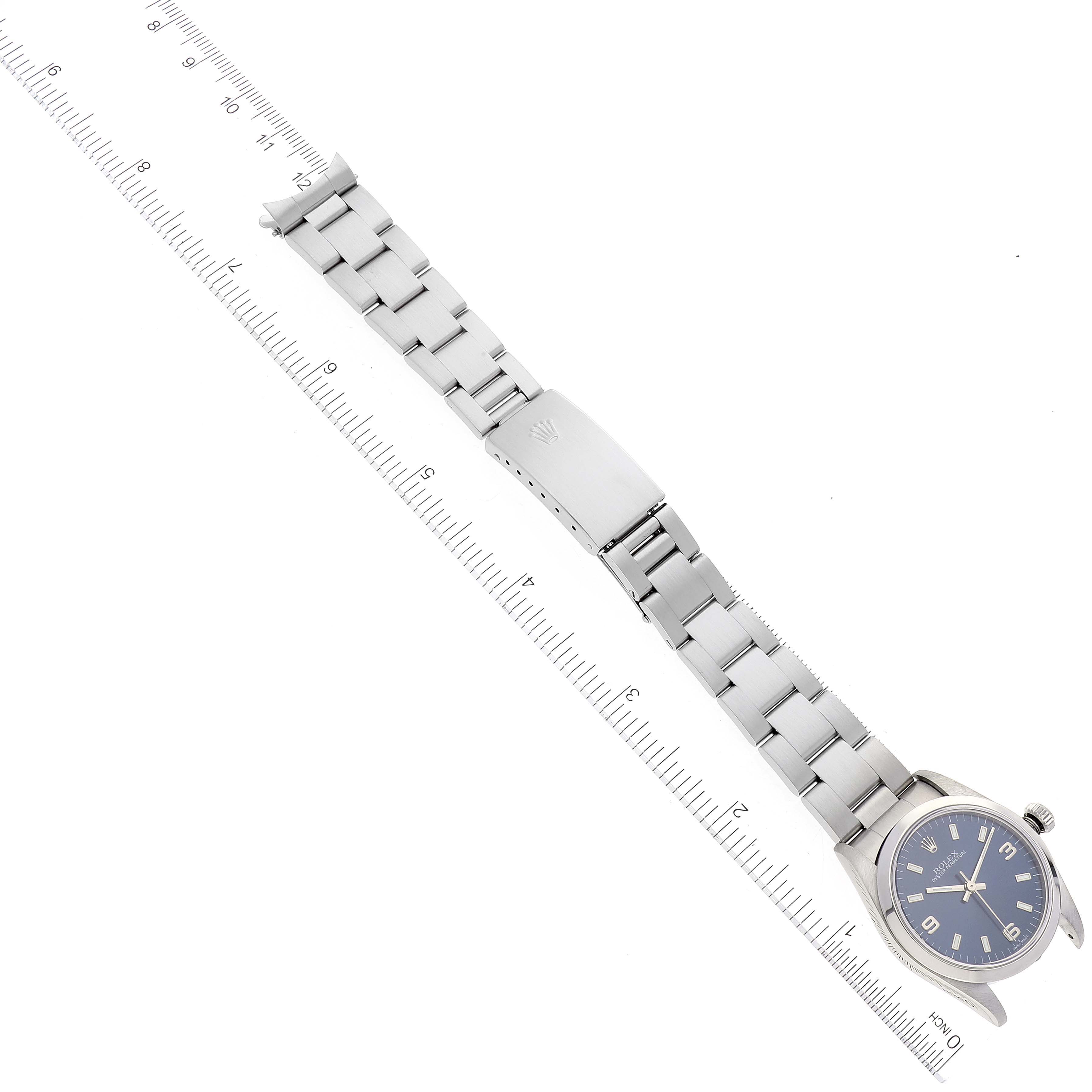 The image shows a Rolex Mid-Size 77080 Women
s Stainless Steel Blue Dial 77080 Women
s Stainless Steel Blue Dial watch laid flat with its bracelet extended, alongside a ruler for measurement.
