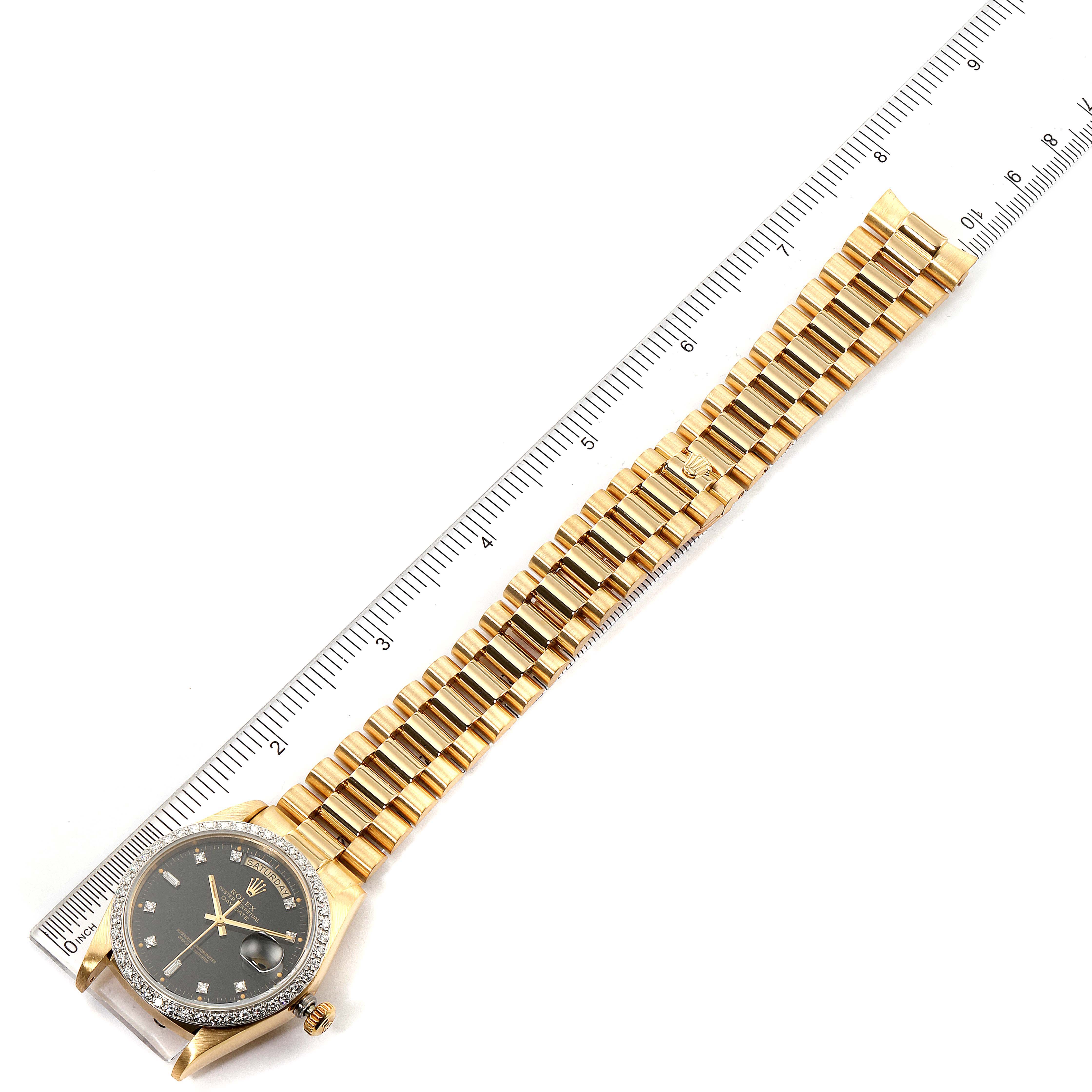 The image shows the Rolex President 18048 Men
s Yellow Gold Black Dial 18048 Men
s Yellow Gold Black Dial watch from a top-down angle, featuring its dial, bezel, and the full length of the bracelet alongside a ruler.