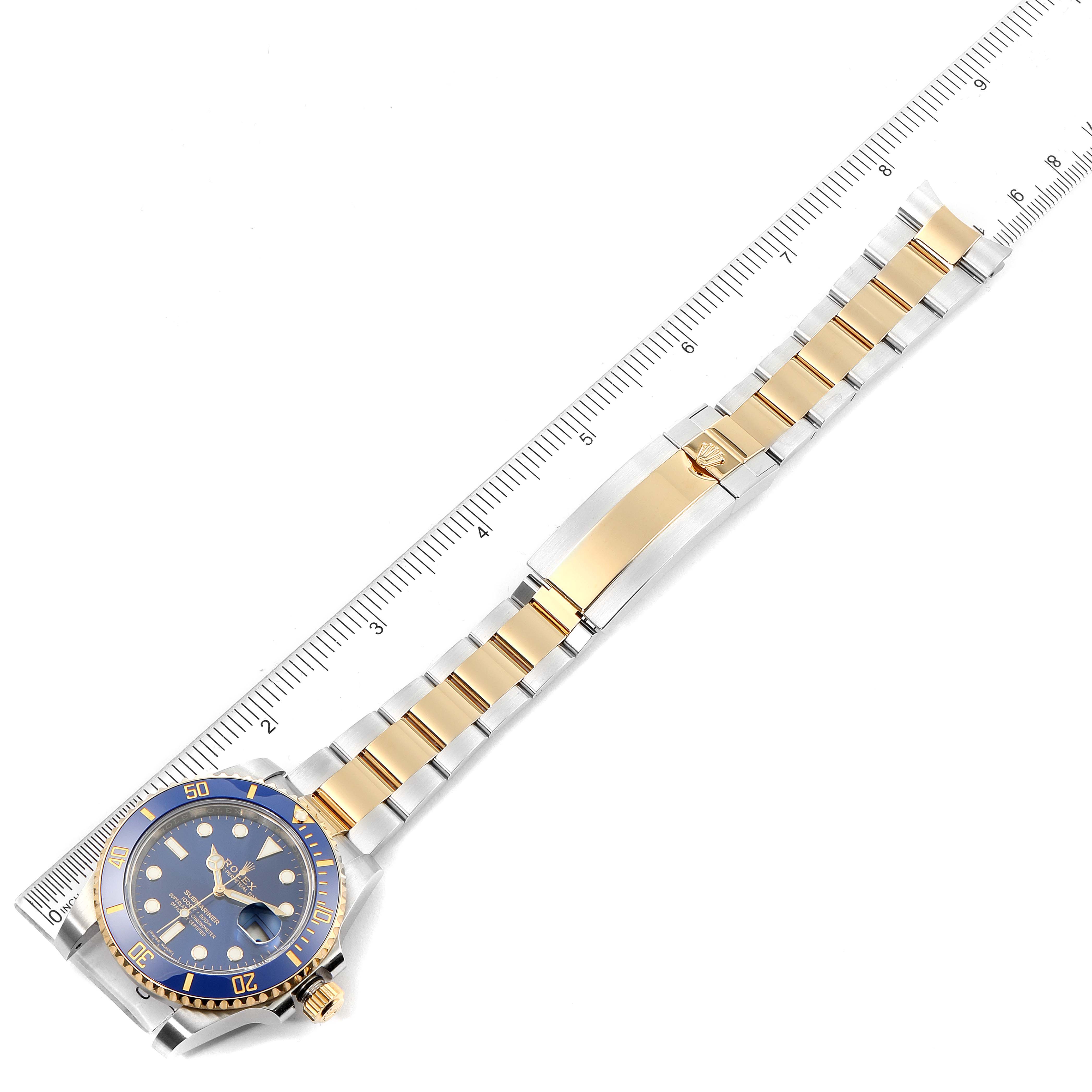The image shows a top-down view of a Rolex Submariner 116613 Men's Steel and Gold (two tone) Blue Dial 116613 Men's Steel and Gold (two tone) Blue Dial watch with a gold and silver bracelet next to a measurement ruler.