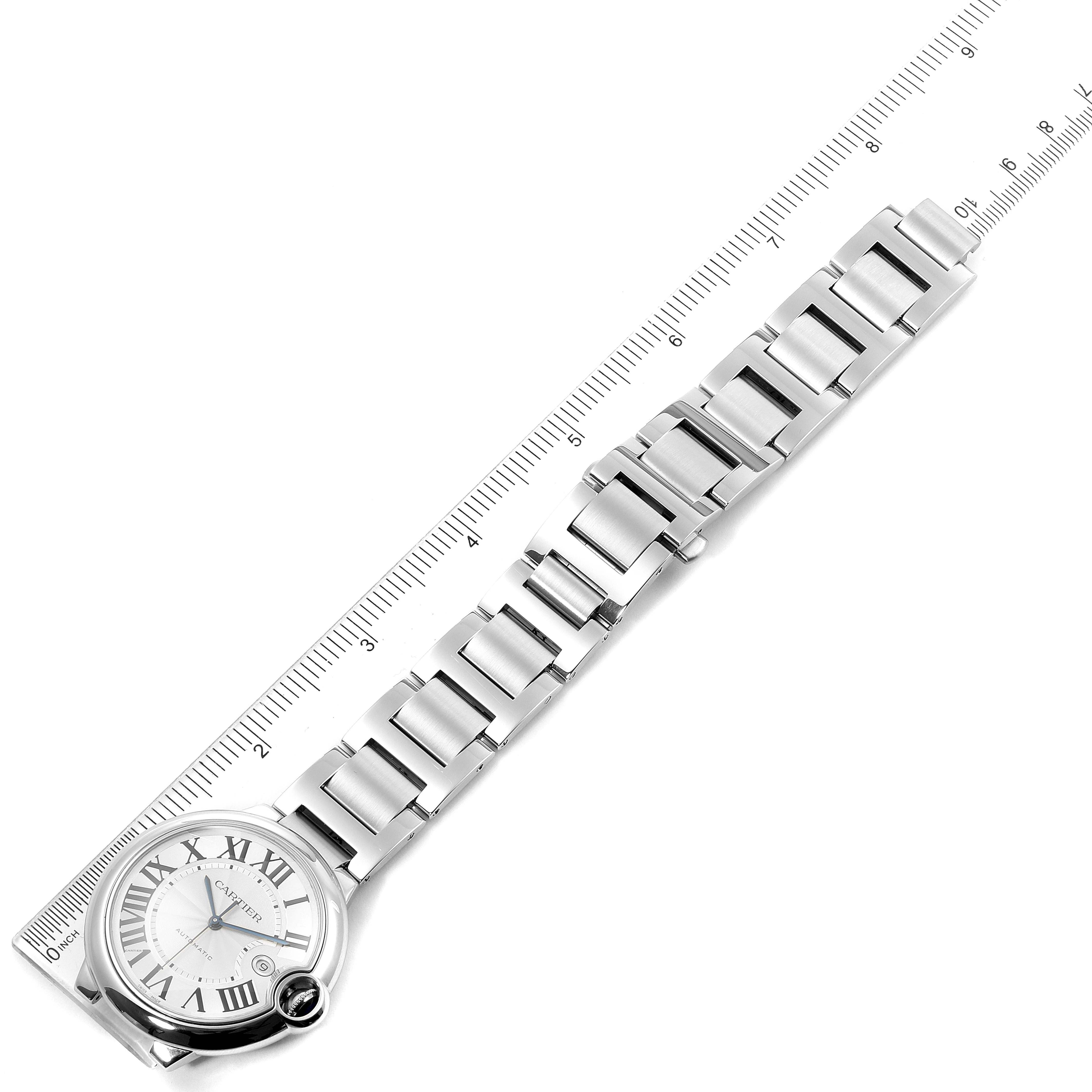 The image shows a top-down view of the Ballon Bleu by Cartier, displaying its face and metal bracelet next to a ruler.