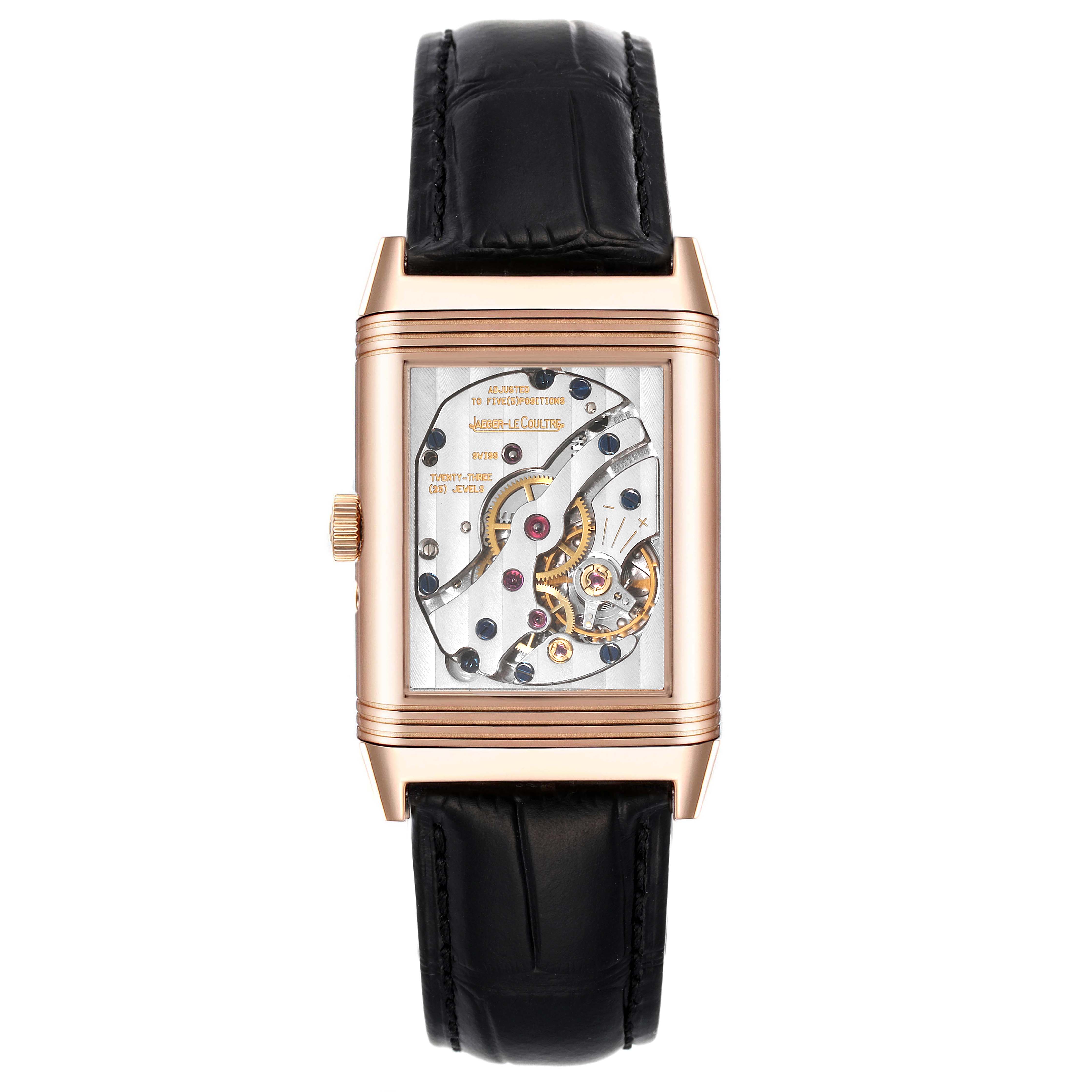 The image shows the back view of a Jaeger-LeCoultre Reverso watch, displaying its intricate movement and components, with a black leather strap.