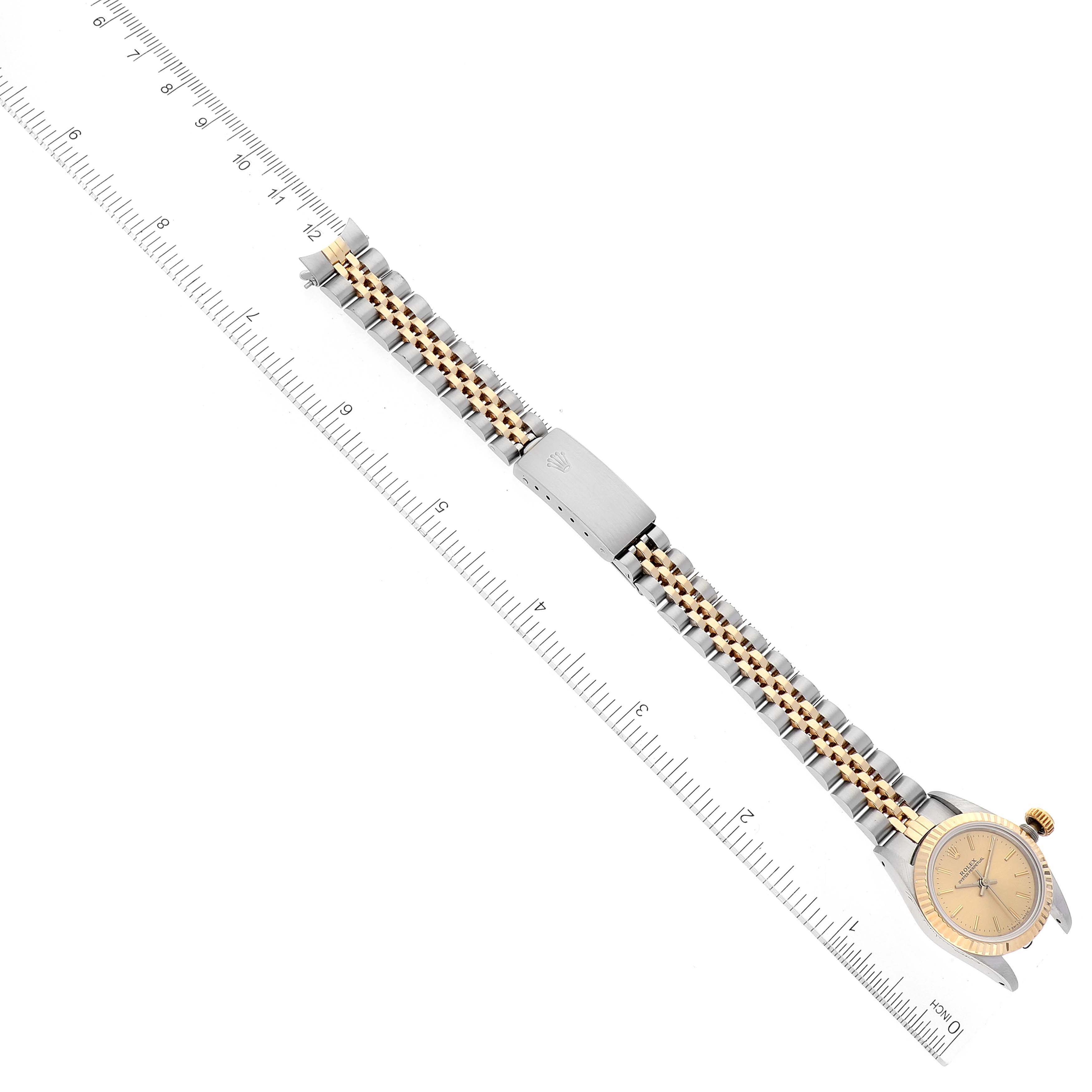 The image shows a top-down view of a Rolex Oyster Perpetual 67193 Women's Steel and Gold (two tone) Champagne Dial 67193 Women's Steel and Gold (two tone) Champagne Dial watch, including its two-tone metal bracelet and clasp, next to a ruler for scale.