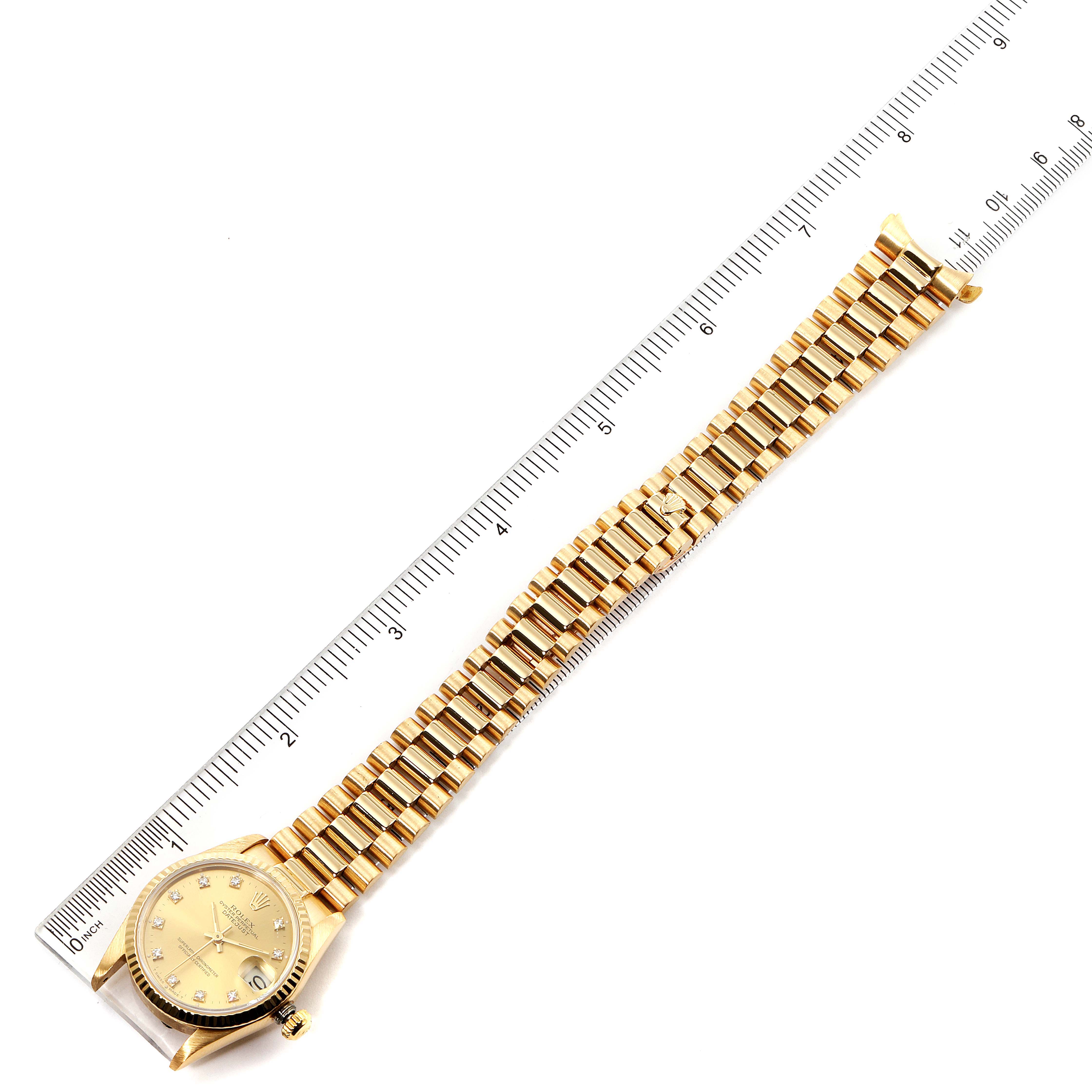 The image shows a Rolex President 68278 Women
s Yellow Gold Champagne Dial 68278 Women
s Yellow Gold Champagne Dial model watch with a gold bracelet laid flat next to a ruler, displaying the full face and strap.