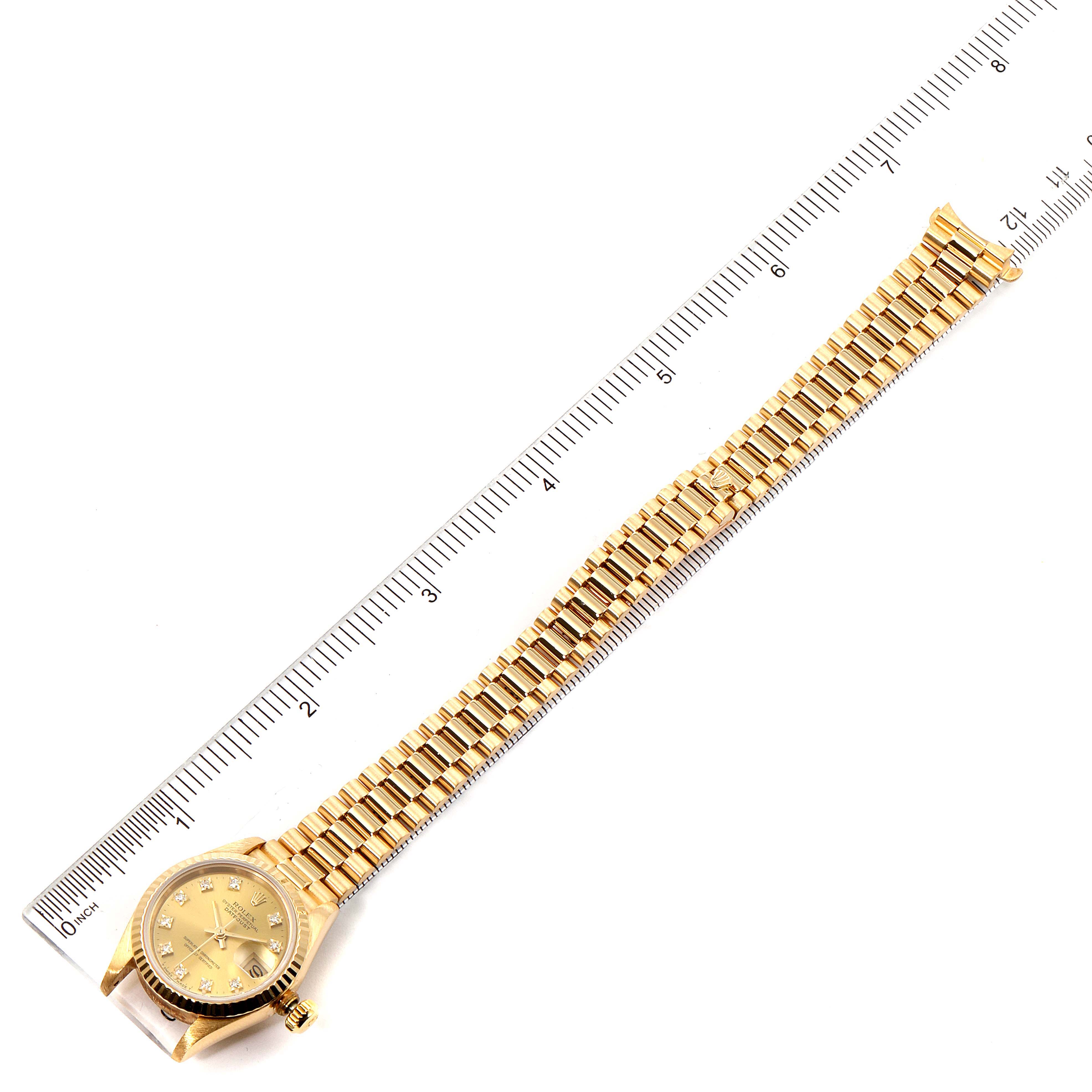 This image shows a top-down view of a Rolex President 69178 Women
s Yellow Gold Champagne Dial 69178 Women
s Yellow Gold Champagne Dial model watch, including the face, bezel, and full bracelet, alongside a ruler.