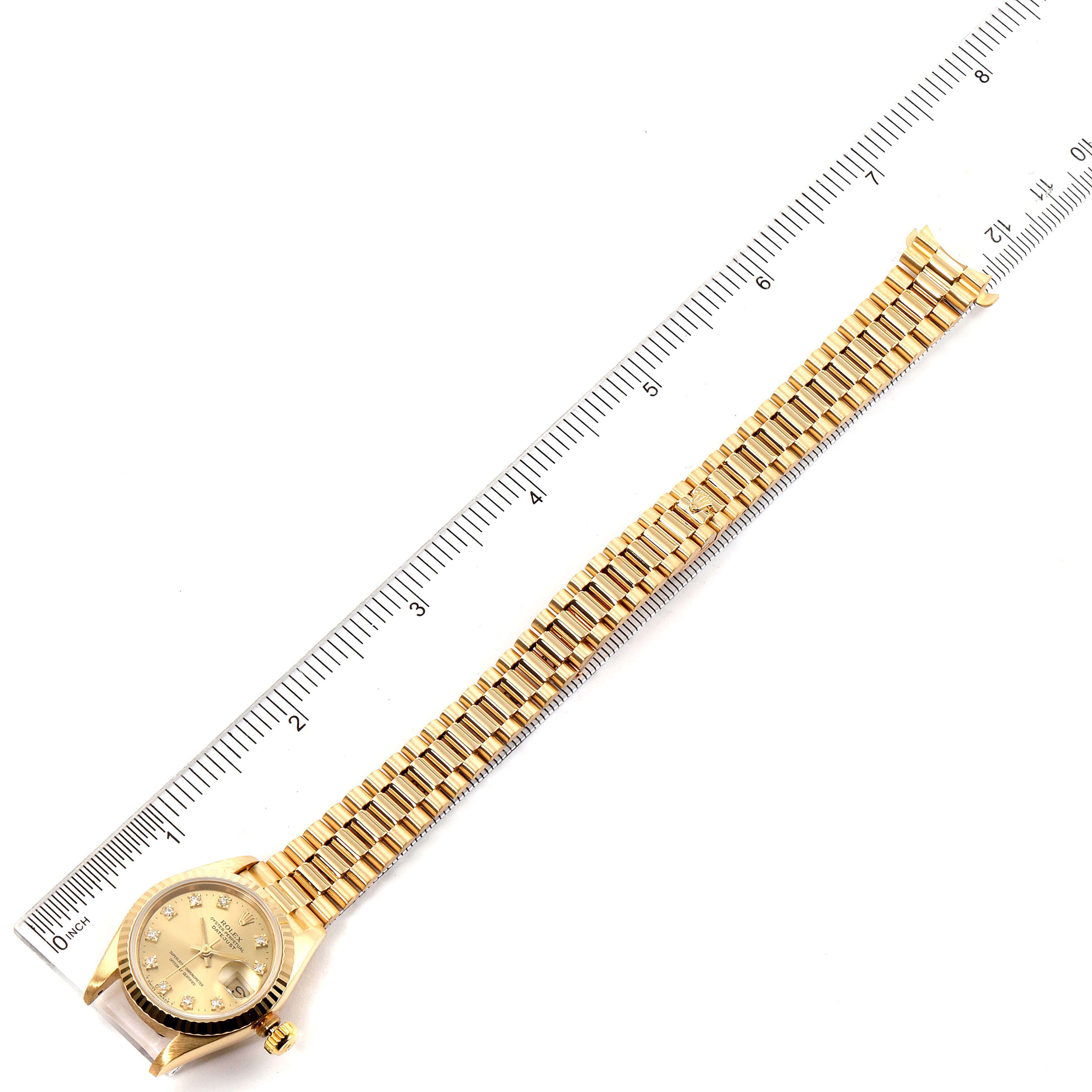 This image shows a Rolex President 69178 Women
s Yellow Gold Champagne Dial 69178 Women
s Yellow Gold Champagne Dial model watch laid flat next to a ruler, displaying its full bracelet and face from a top-down angle.