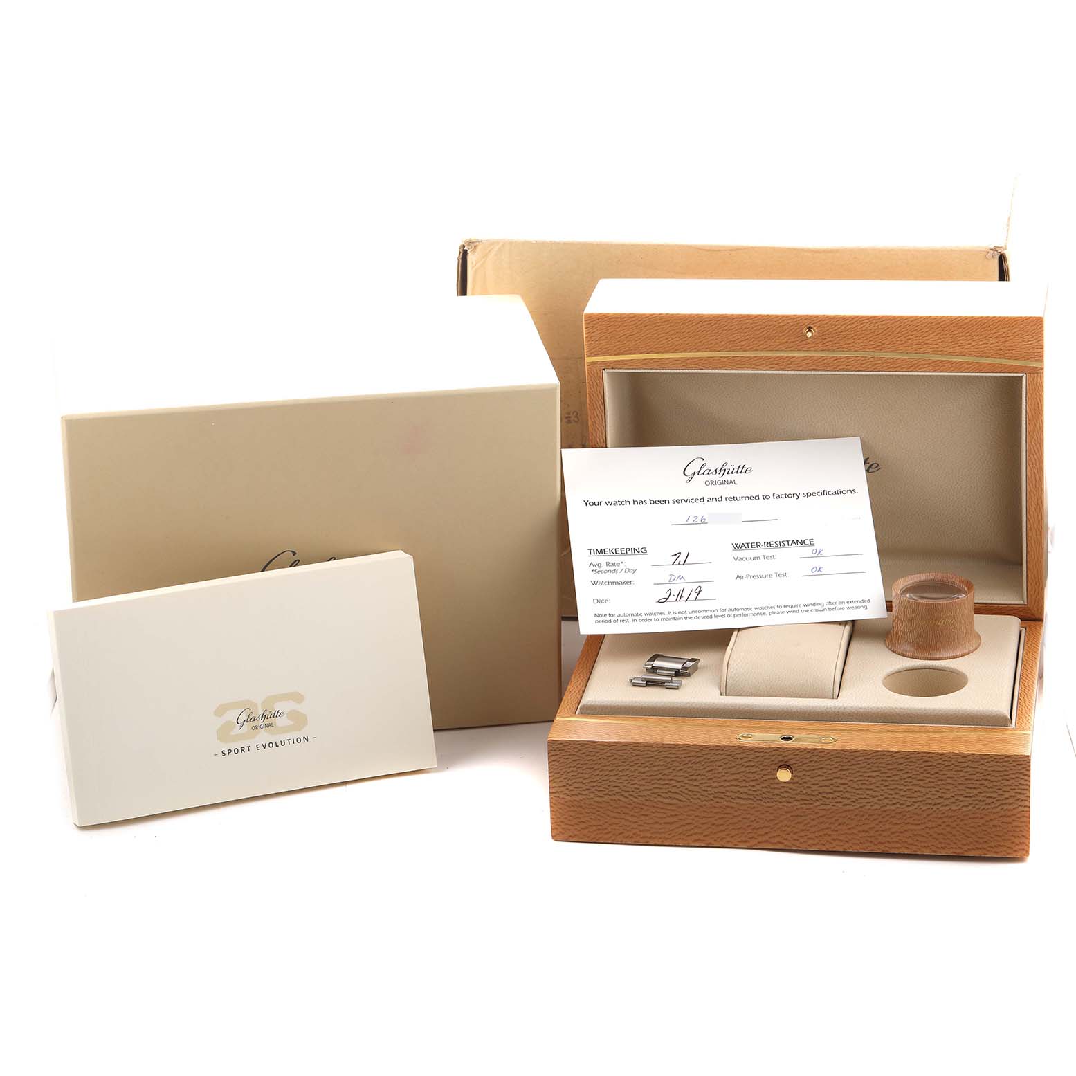 The image shows a Glashütte Original watch box with accessories, including a loupe, spare links, and documentation.