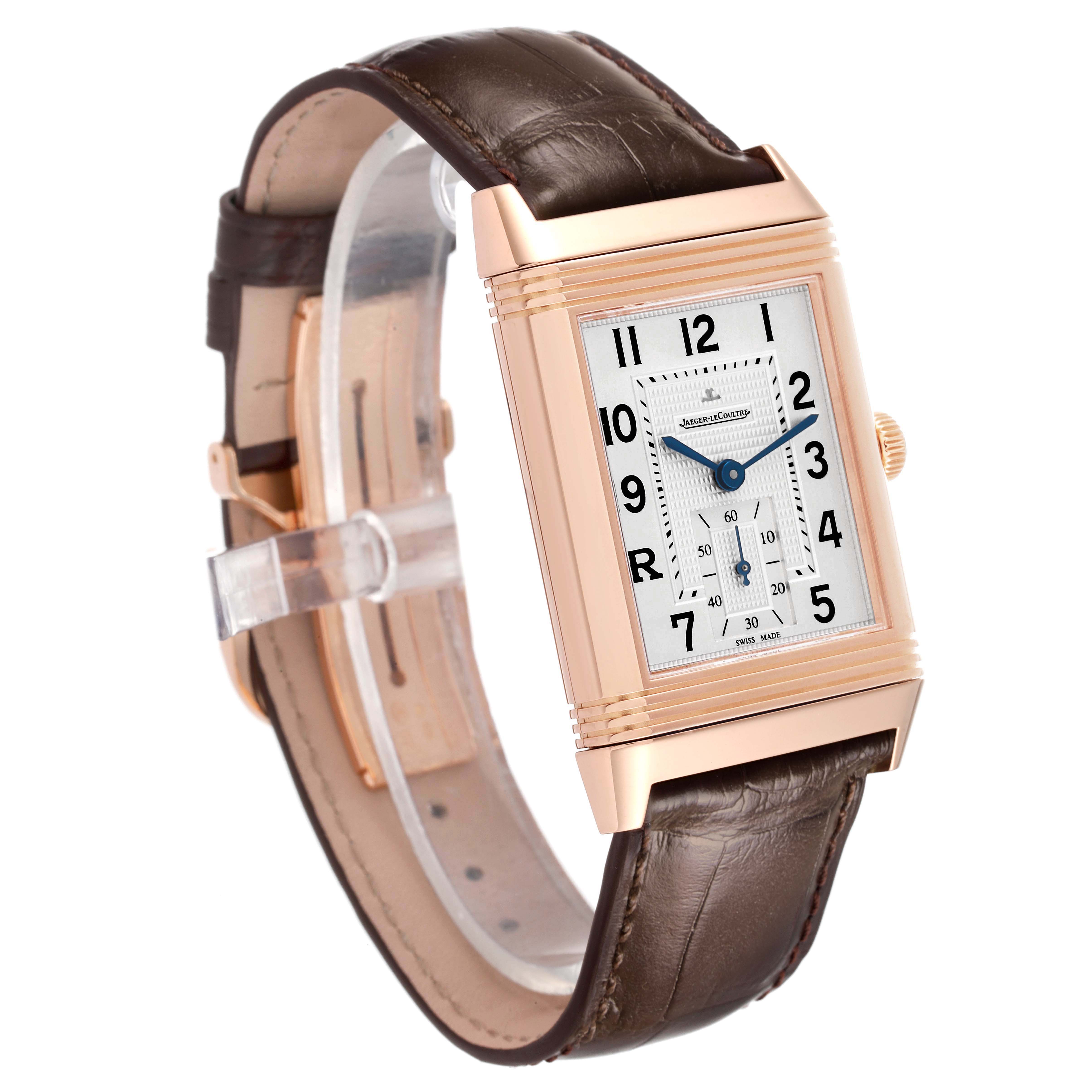The Jaeger-LeCoultre Reverso watch is shown at a slight angle, highlighting its rectangular face, brown leather strap, and gold case.