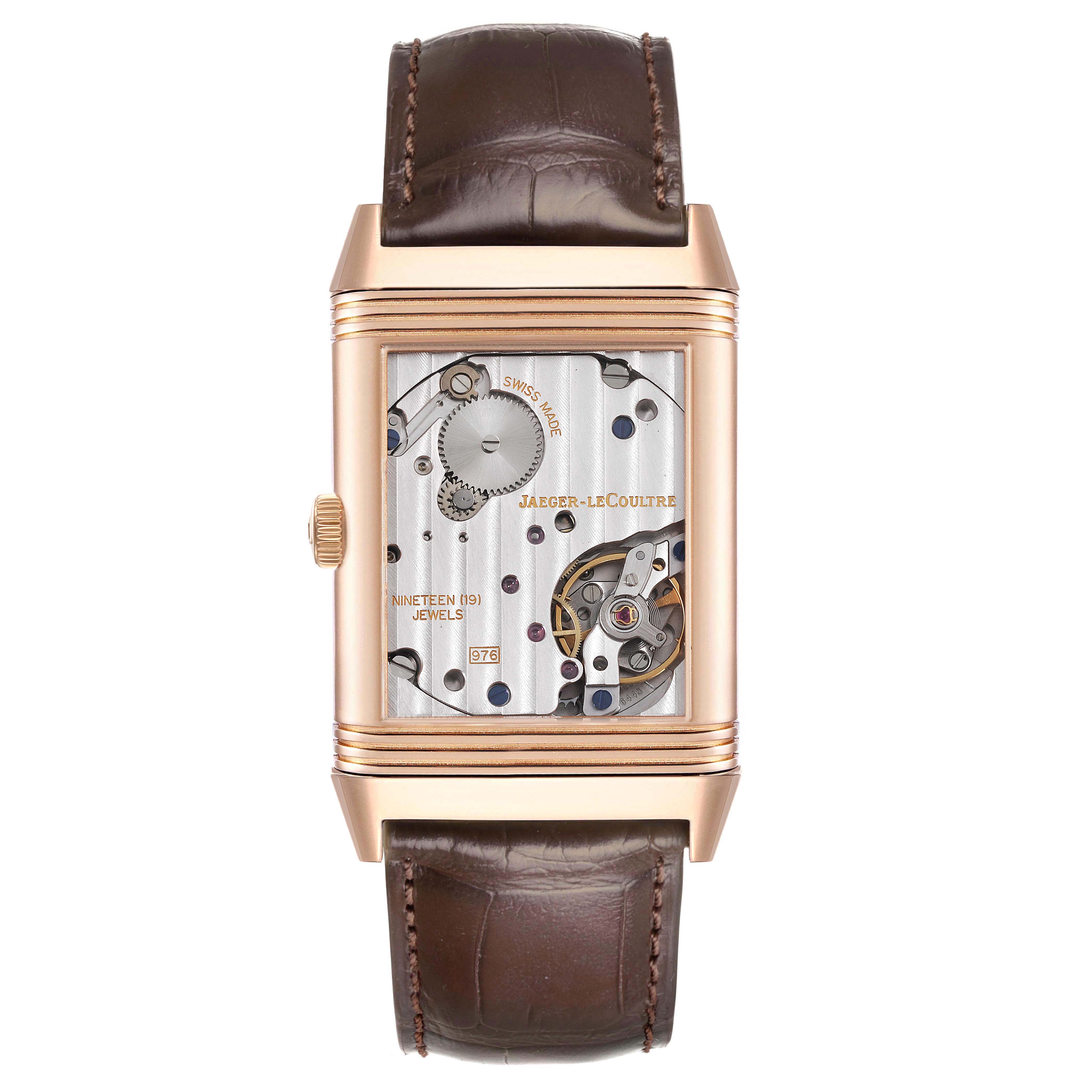 The Jaeger-LeCoultre Reverso watch is shown from the front, displaying the intricate internal movement with visible gears and jewels.