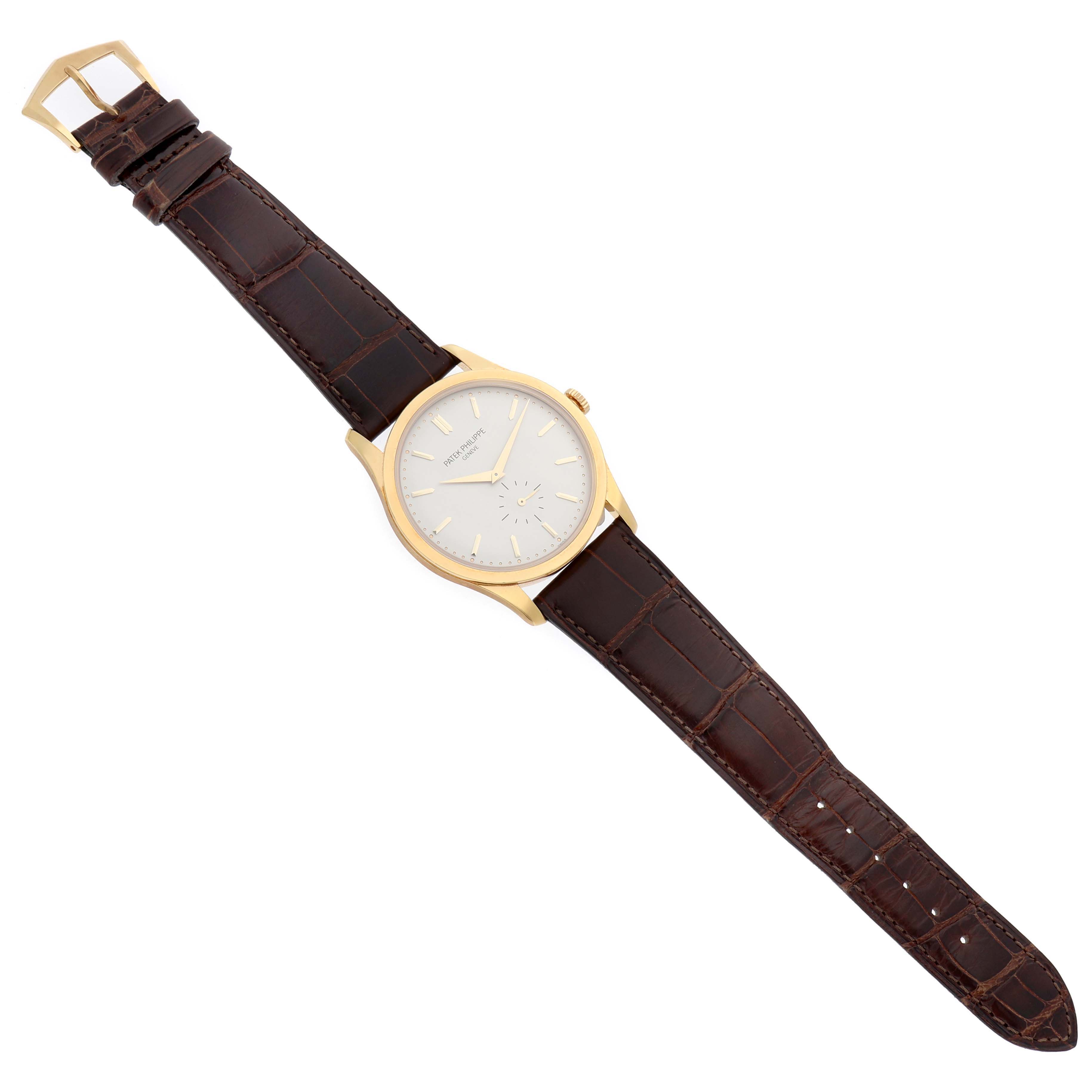 The Patek Philippe Calatrava 5196J Men's Yellow Gold Silver Dial watch is shown from a top-down angle, displaying its dial, case, crown, and brown leather strap.