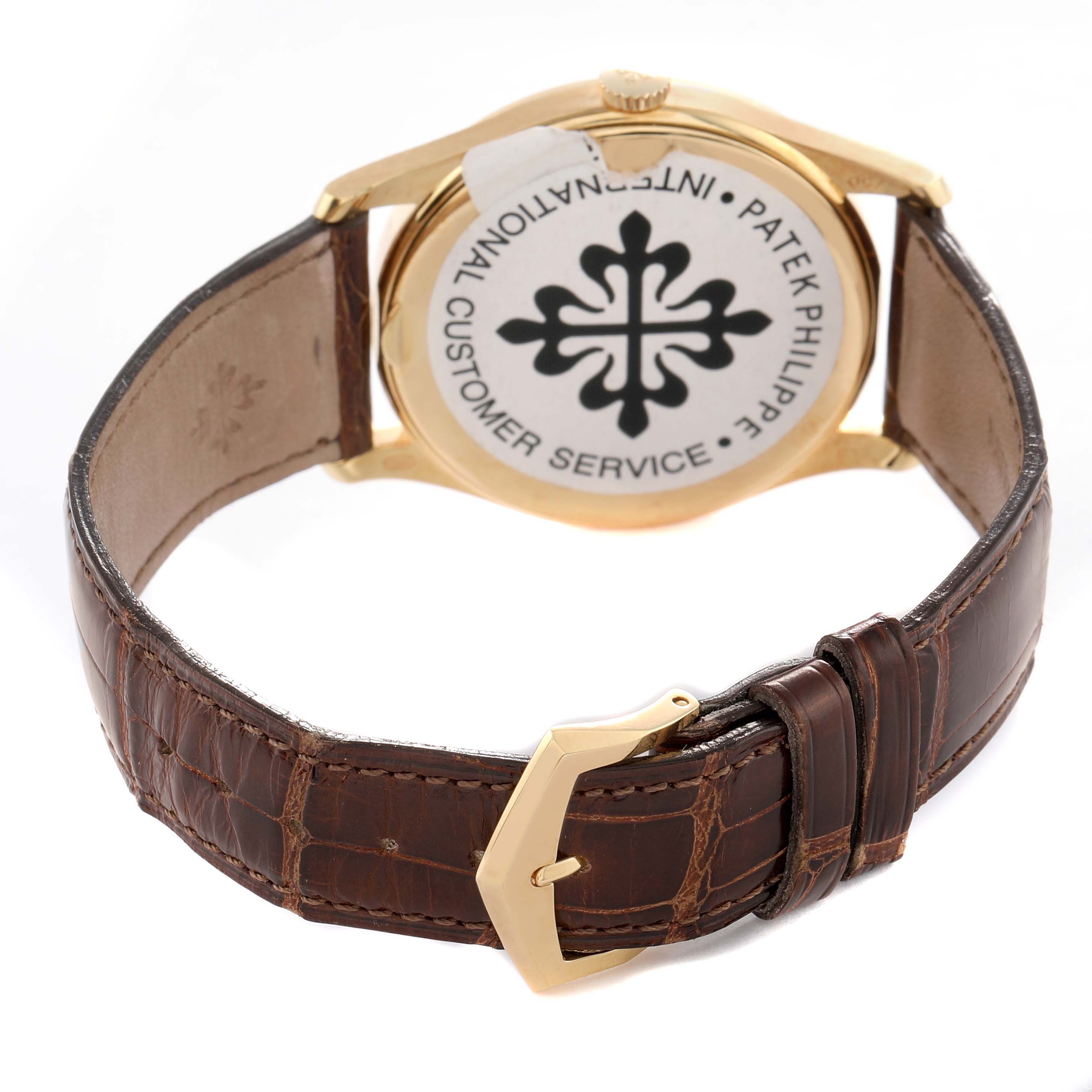 The image shows the back view of a Patek Philippe Calatrava 5196J Men's Yellow Gold Silver Dial watch, highlighting the case back, brown leather strap, and gold buckle.