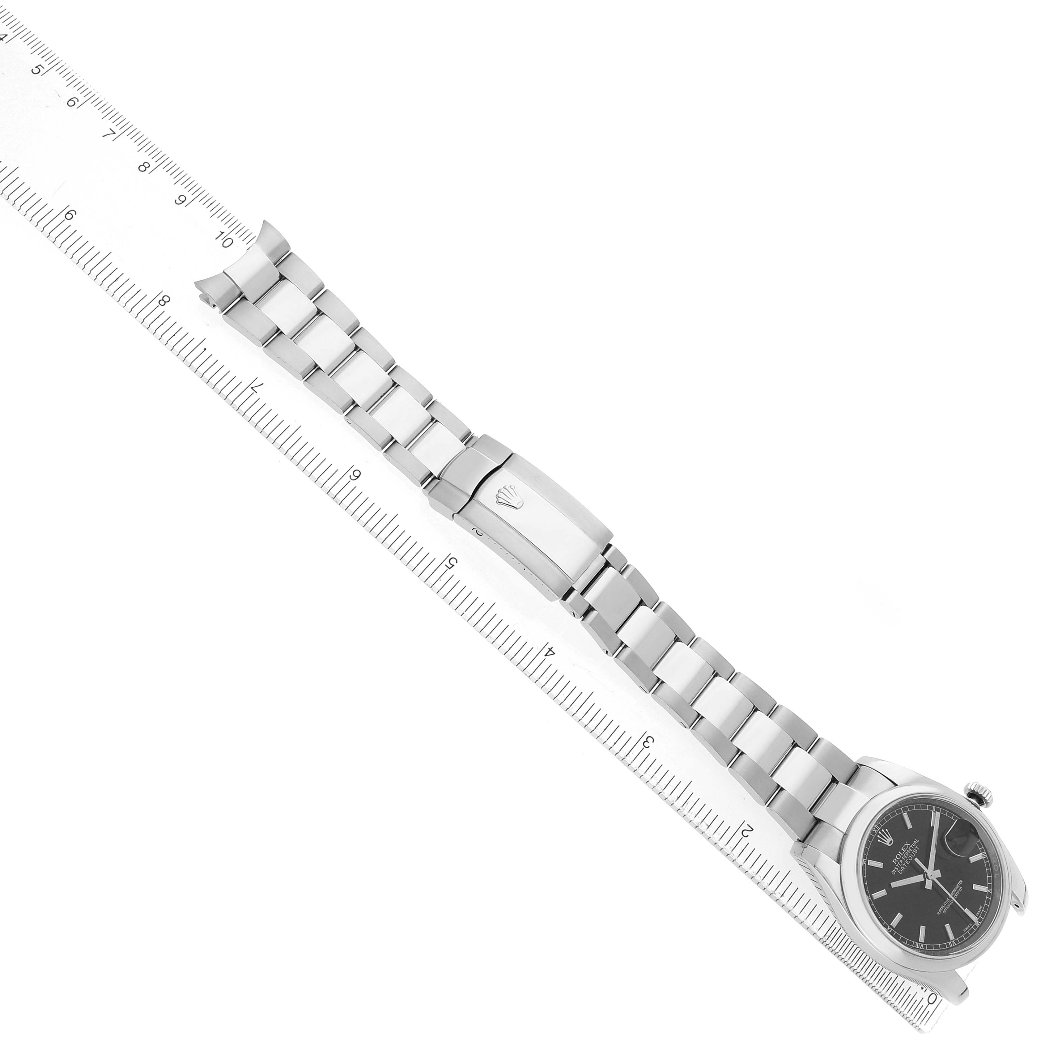 The Rolex Datejust 116200 Men's Stainless Steel Black Dial watch is shown from a top angle, displaying its face, bracelet, and clasp alongside a ruler for scale.