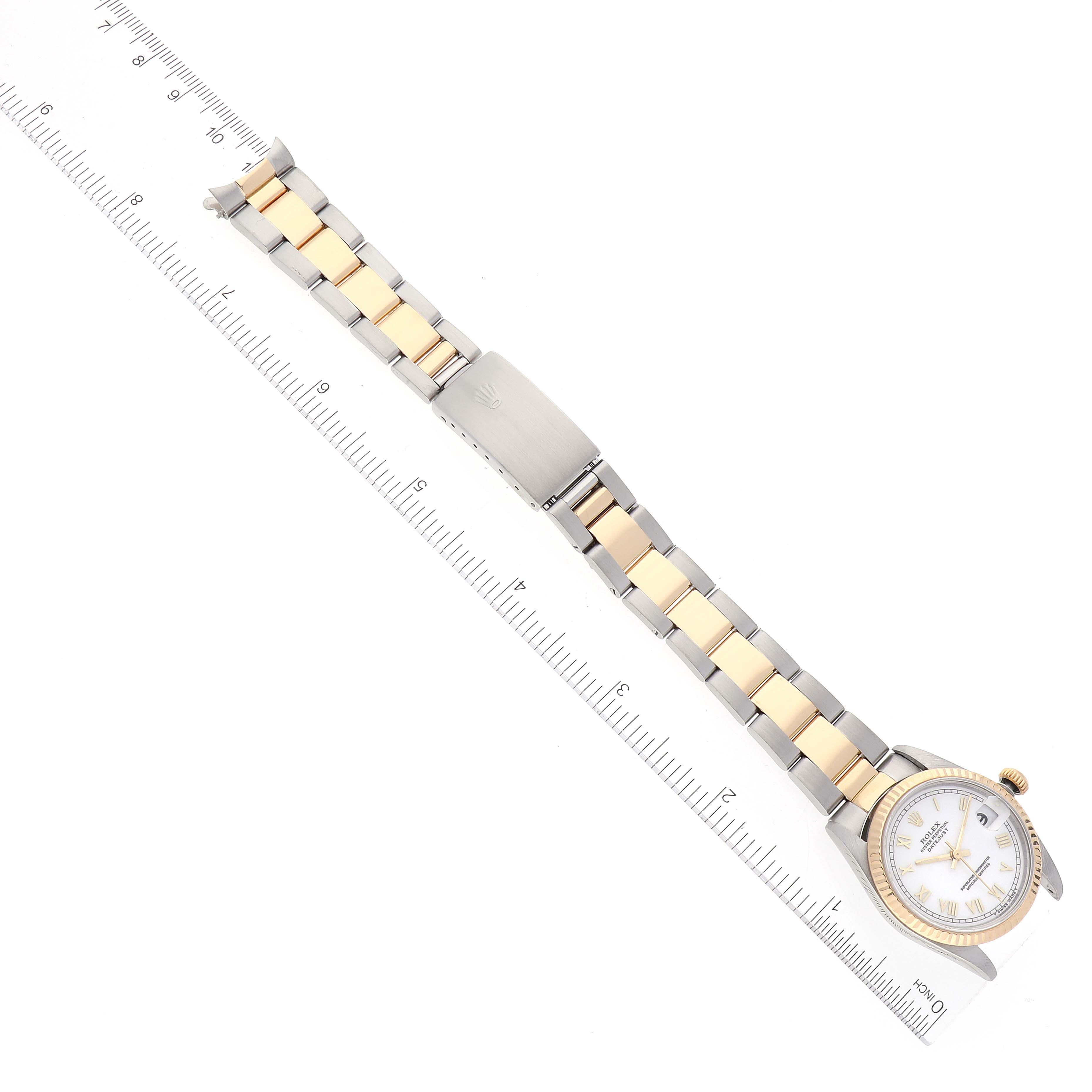 The image shows a Rolex Mid-Size 78273 Women
s Steel and Gold (two tone) White Dial 78273 Women
s Steel and Gold (two tone) White Dial watch from a top view, highlighting the full bracelet, clasp, and face alongside a ruler.
