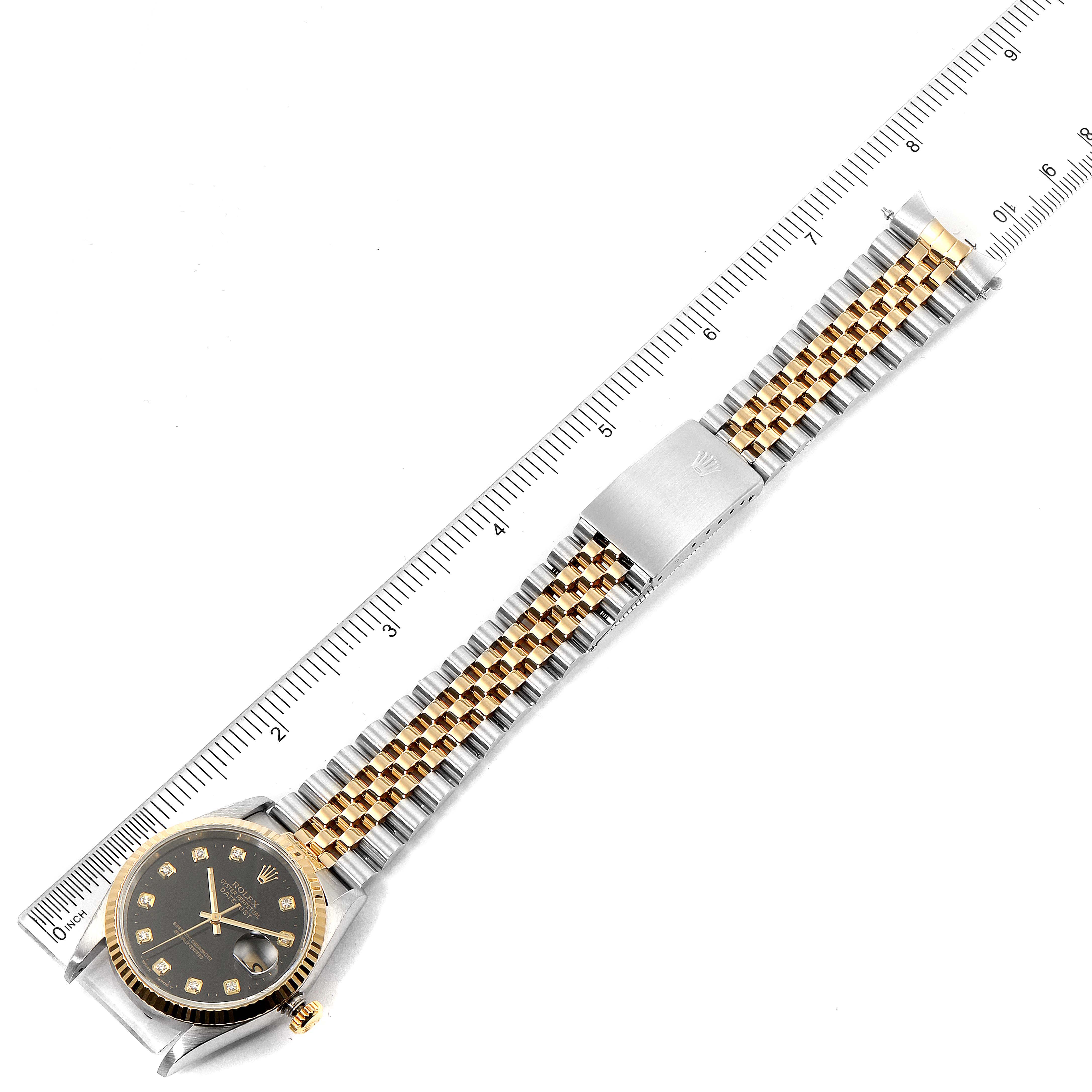 The image shows a top-down view of a Rolex Datejust 16233 Men
s Steel and Gold (two tone) Black Dial 16233 Men
s Steel and Gold (two tone) Black Dial watch with a two-tone metal strap and a ruler for scale.