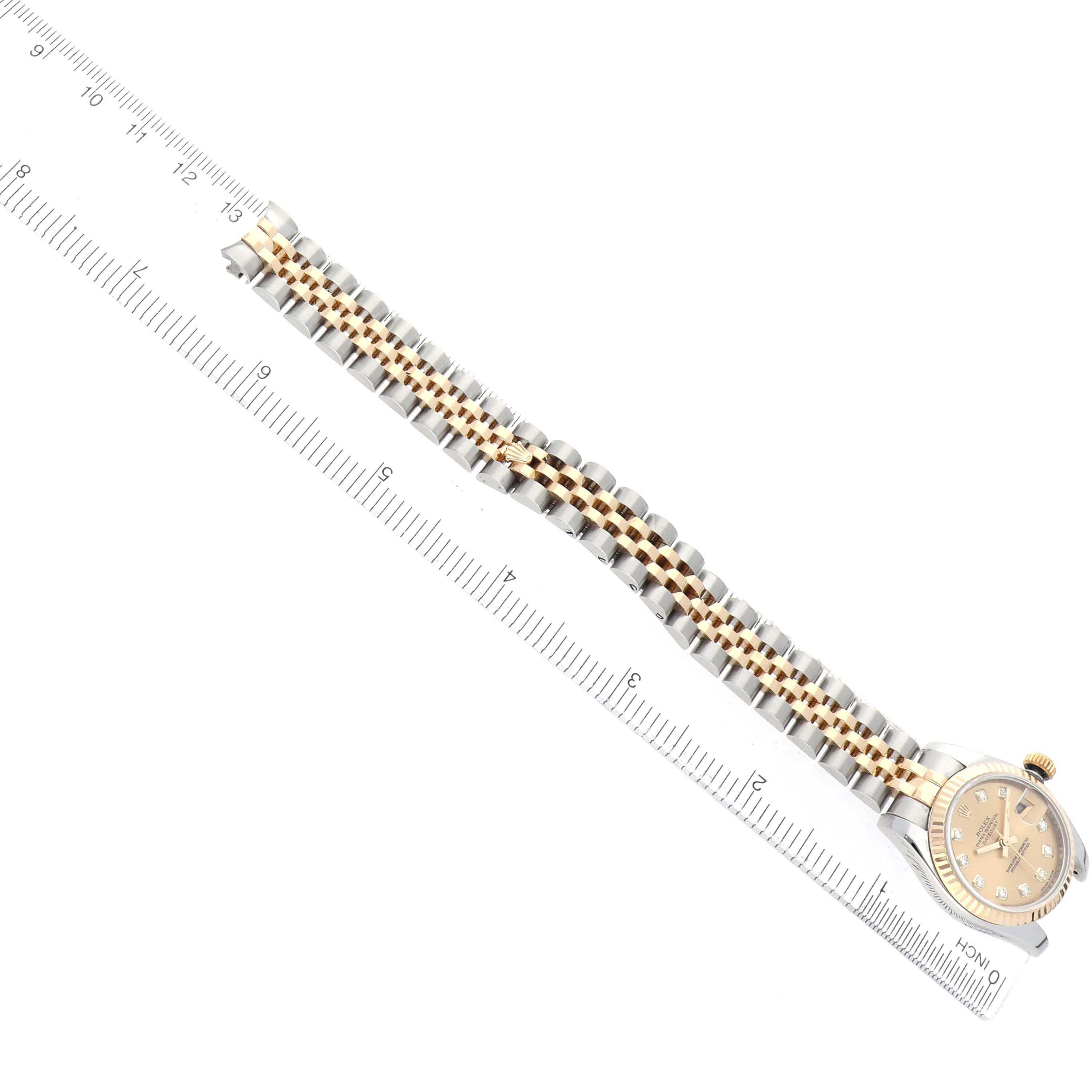 The Rolex Datejust 179173 Women's Steel and Gold (two tone) Champagne Dial watch is shown from an overhead angle, highlighting the band and watch face beside a measuring ruler.