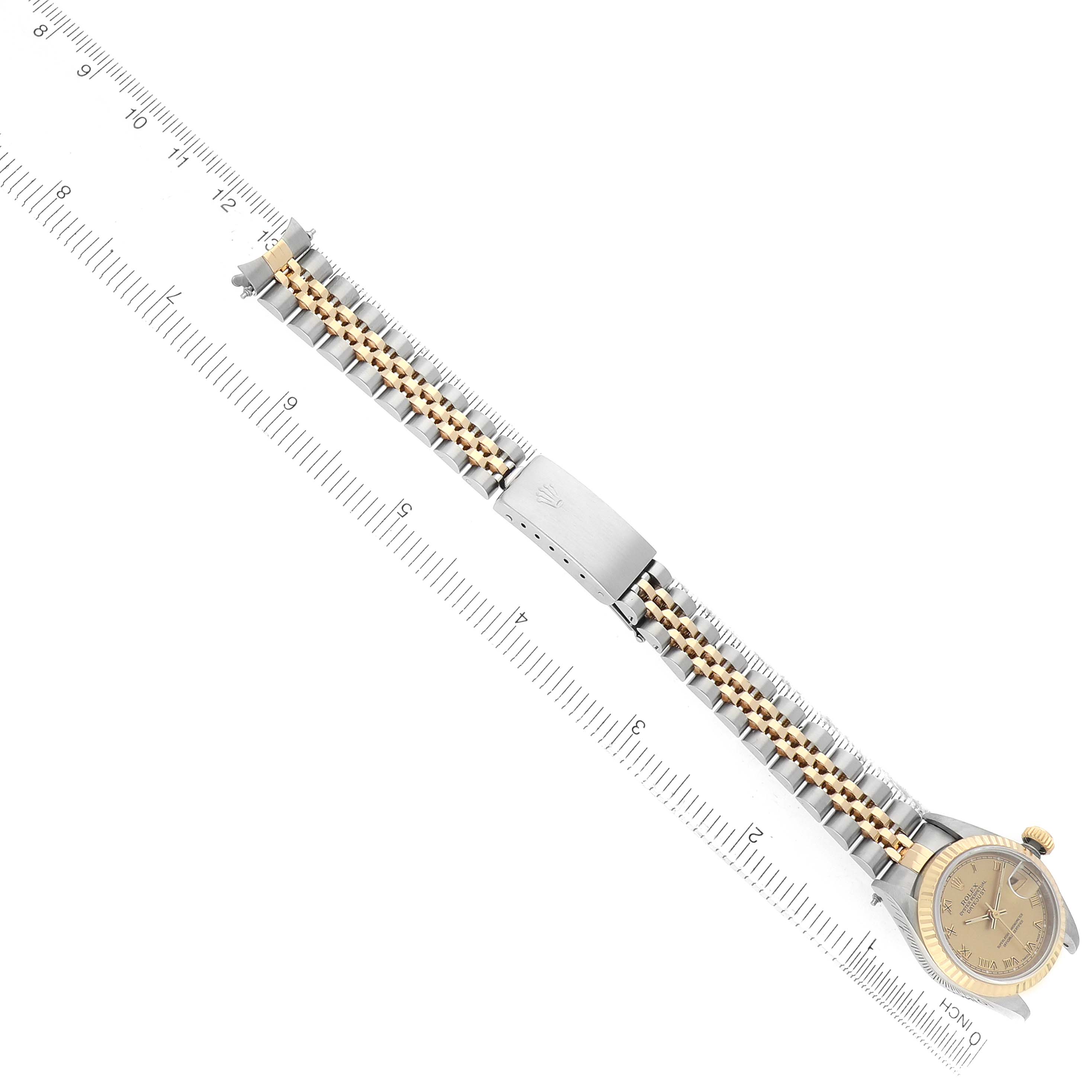 The Rolex Datejust 69173 Women's Steel and Gold (two tone) Champagne Dial watch is shown from an angled top view, featuring the two-tone bracelet and clasp alongside a measuring ruler.
