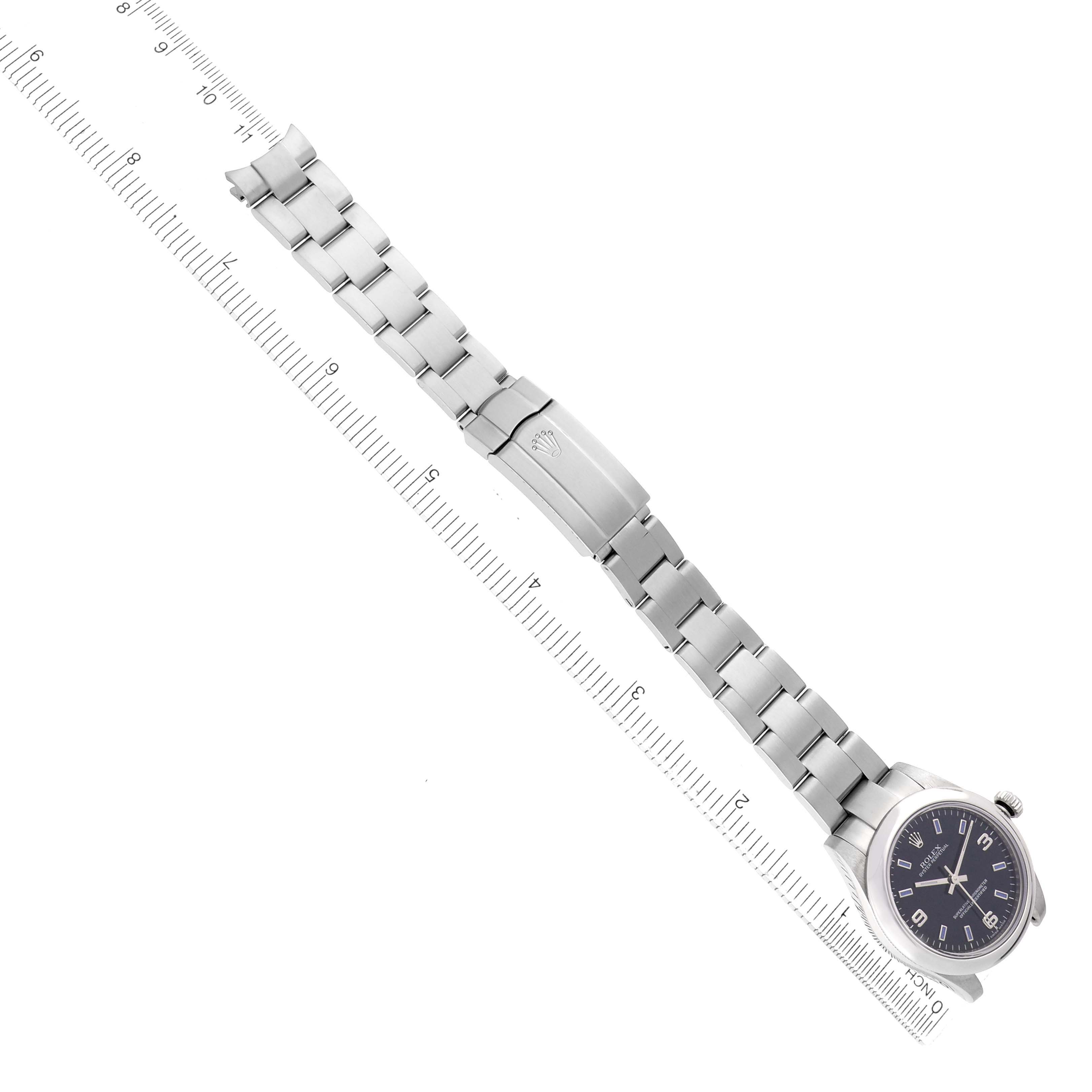 The Rolex Mid-Size 177200 Women's Stainless Steel Black Dial watch is shown from an overhead angle, displaying the full band and face against a ruler.