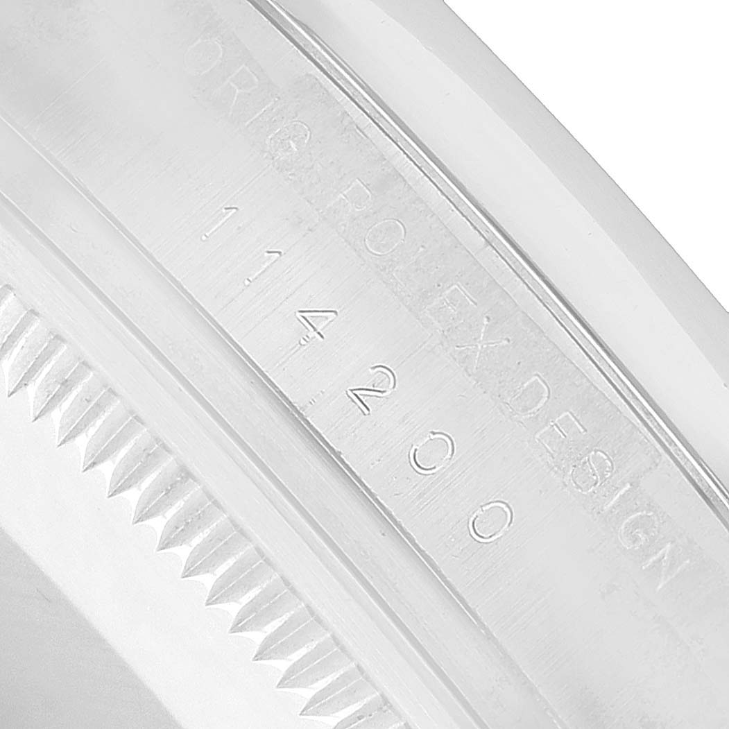 The image shows the engraved side of the bezel of a Rolex Oyster Perpetual 114200 Men's Stainless Steel Purple Dial, highlighting the model number.