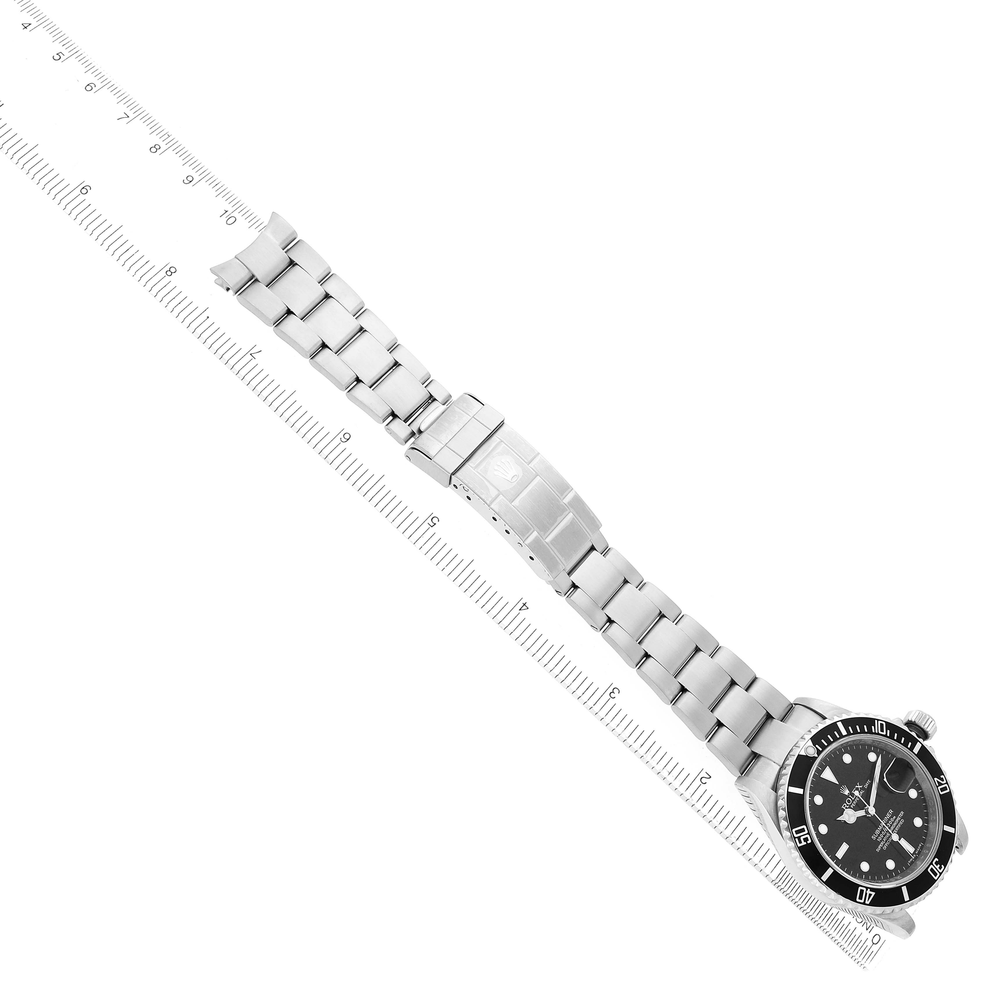The Rolex Submariner 16610 Men's Stainless Steel Black Dial watch is laid diagonally, showing the bracelet, clasp, and face with a ruler underneath.