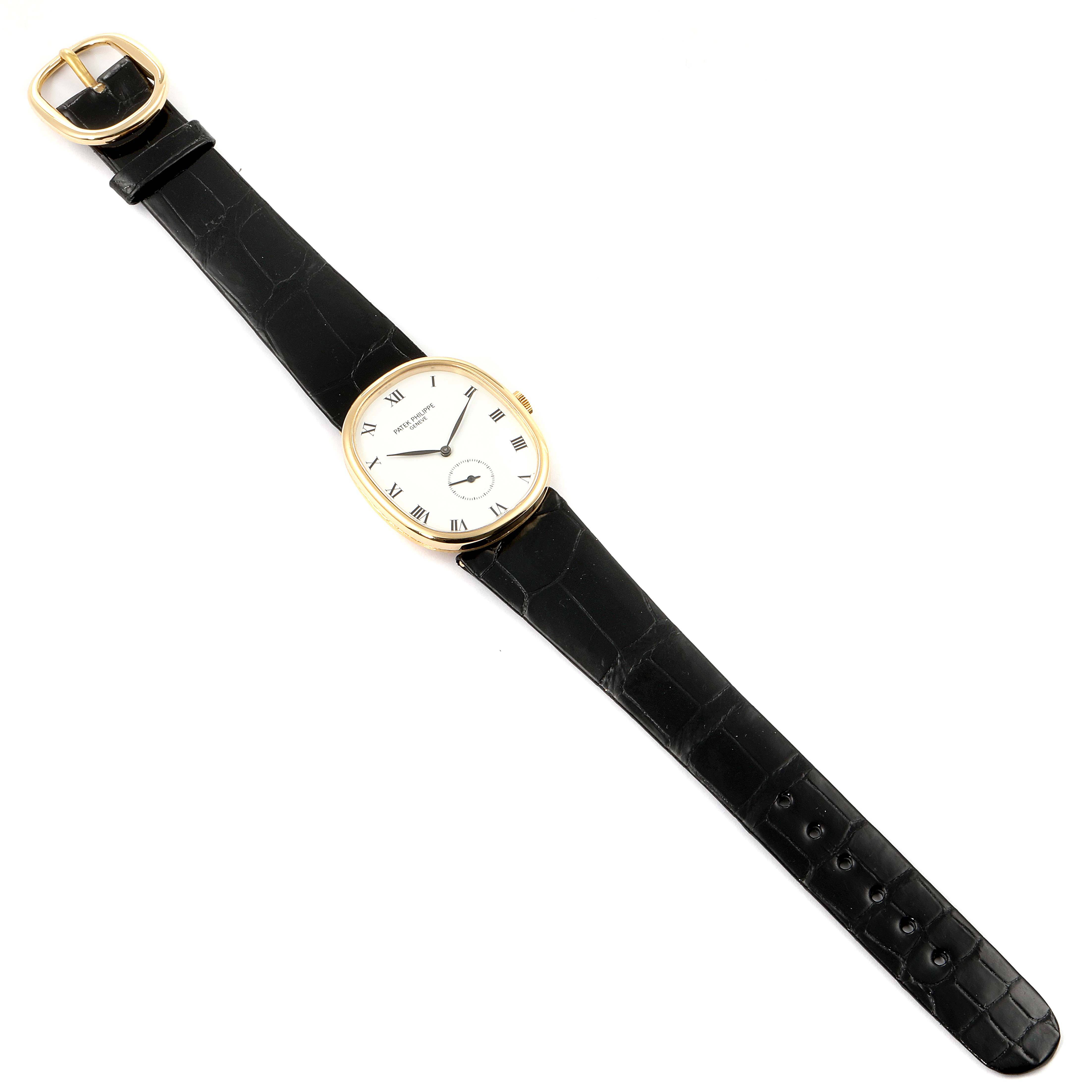 The image shows a Patek Philippe Golden Ellipse 3948 Men's Yellow Gold White Dial 3948 Men's Yellow Gold White Dial watch from a top-down angle, featuring a black strap and a gold-toned oval case.