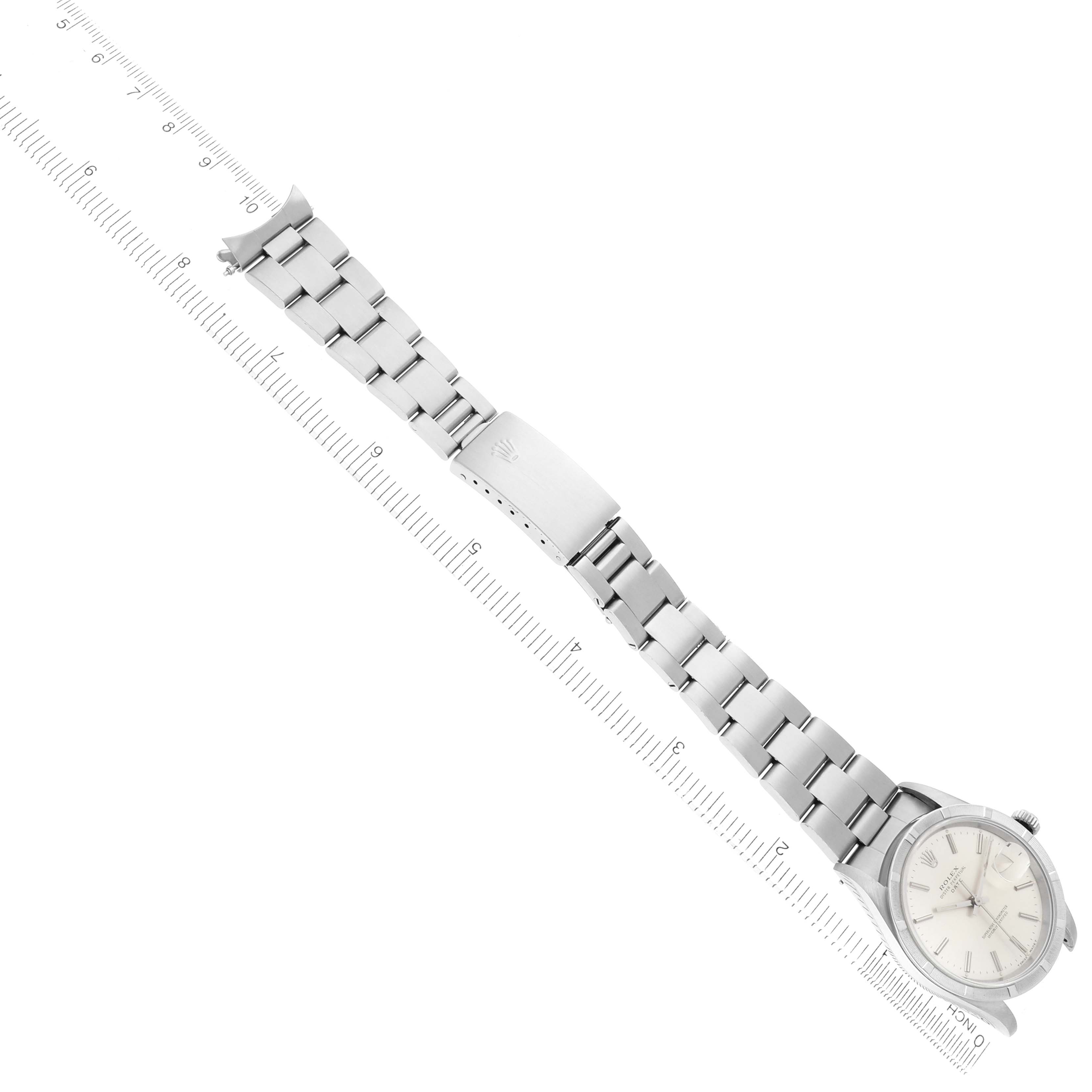 The Rolex Date 15210 Men's Stainless Steel Silver Dial watch is shown from an overhead angle, displaying the entire bracelet and clasp, with a ruler for scale.