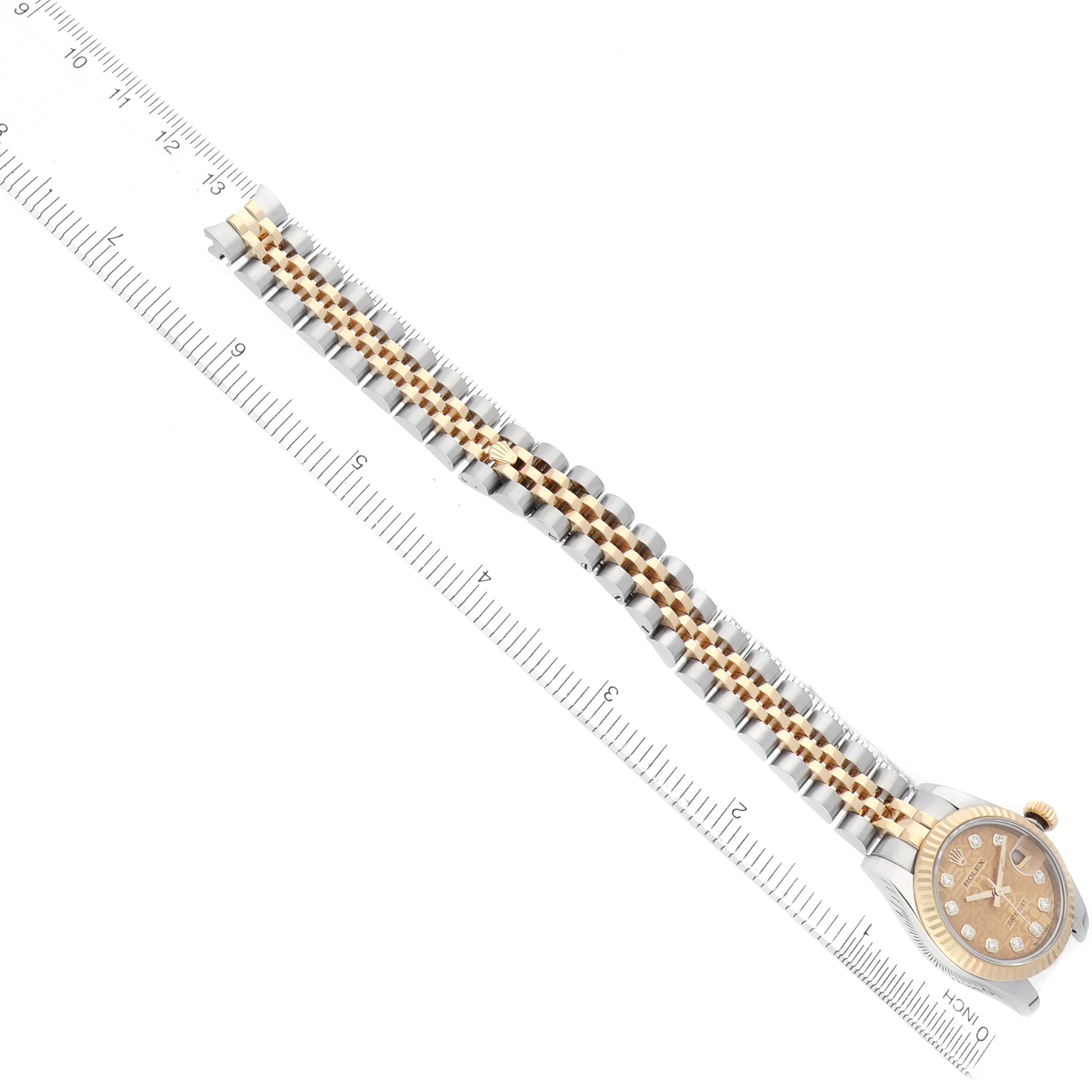 The Rolex Datejust 179173 Women's Steel and Gold (two tone) Champagne Dial watch is shown from a top angle, displaying its face and metal link bracelet alongside a measuring ruler.
