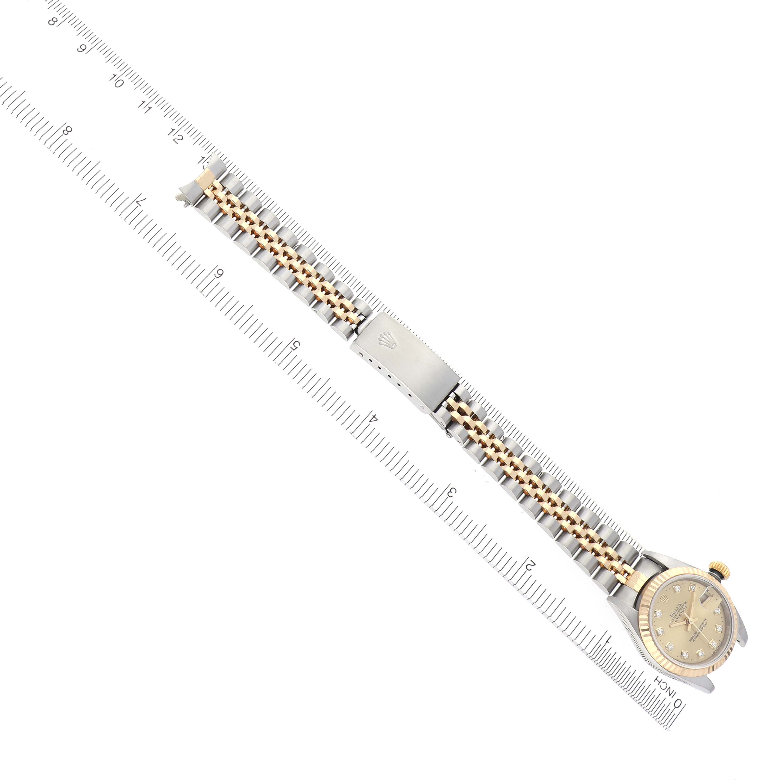 The image shows a Rolex Datejust 79173 Women
s Steel and Gold (two tone) Champagne Dial 79173 Women
s Steel and Gold (two tone) Champagne Dial watch from a top-down angle, highlighting the bracelet and watch face beside a ruler.