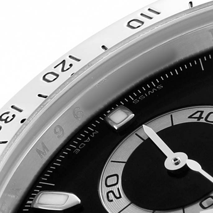 The image shows a close-up of the Rolex Daytona 116520 Men's Stainless Steel Black Dial watch's bezel, dial, and hour markers at an angle highlighting its detailing.