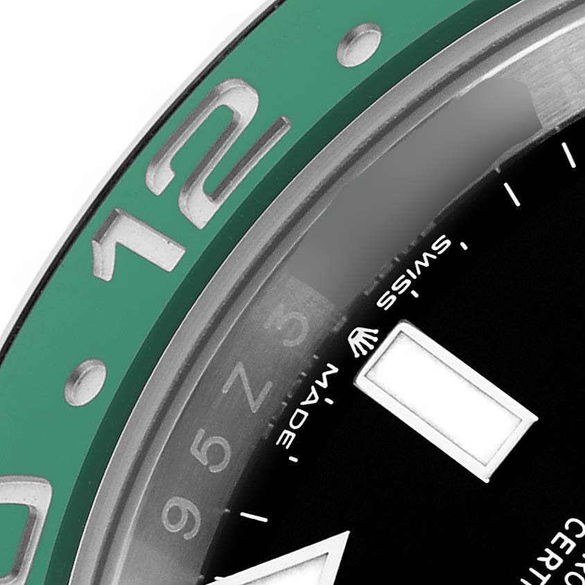 The image shows a close-up of the bezel and part of the dial of a Rolex GMT-Master 126720VTNR Men's Stainless Steel Black Dial 126720VTNR Men's Stainless Steel Black Dial watch, emphasizing the green bezel and 12 o'clock marker.